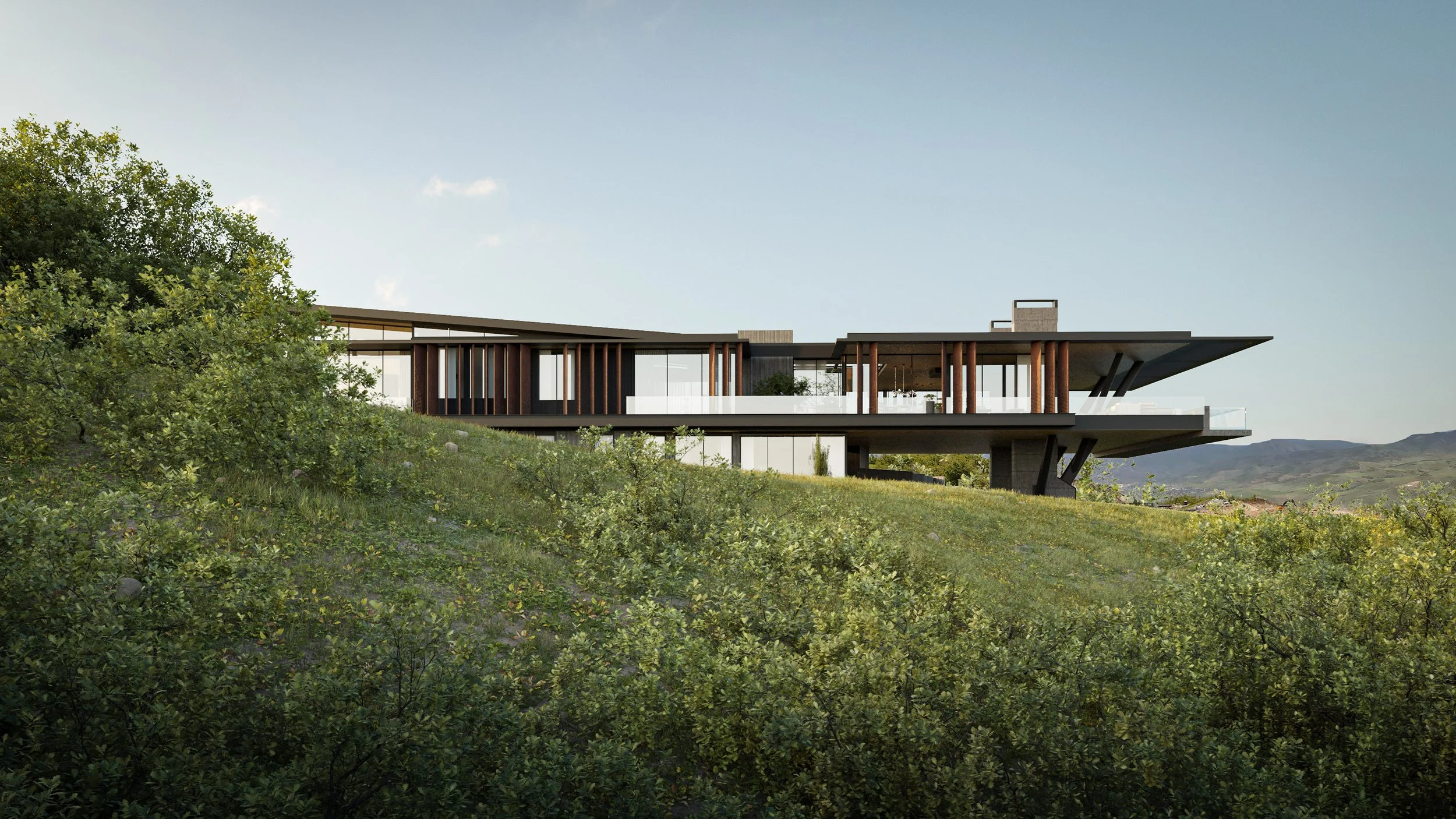 Modern house with large glass windows and wooden columns, situated on a grassy hillside with green shrubs, hillside in background, under a clear blue sky.