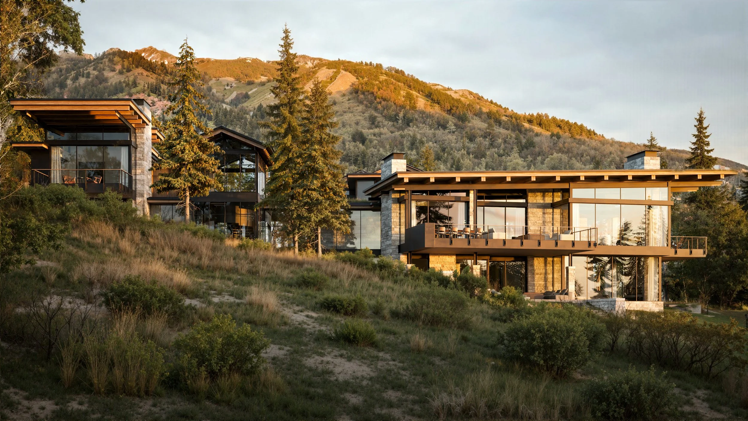 Modern multi-level house with large glass windows and wooden accents, situated on a hillside with trees and mountains in the background at sunset.