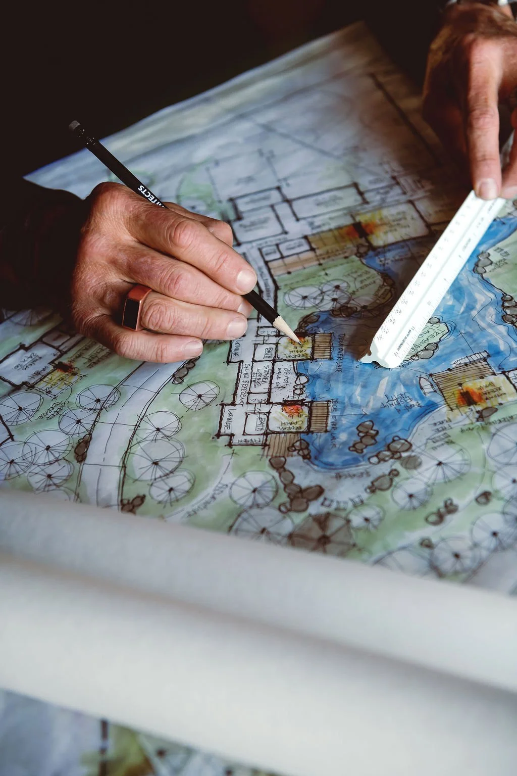 A person is drawing and planning on a detailed architectural or landscape blueprint using a ruler and pencil.