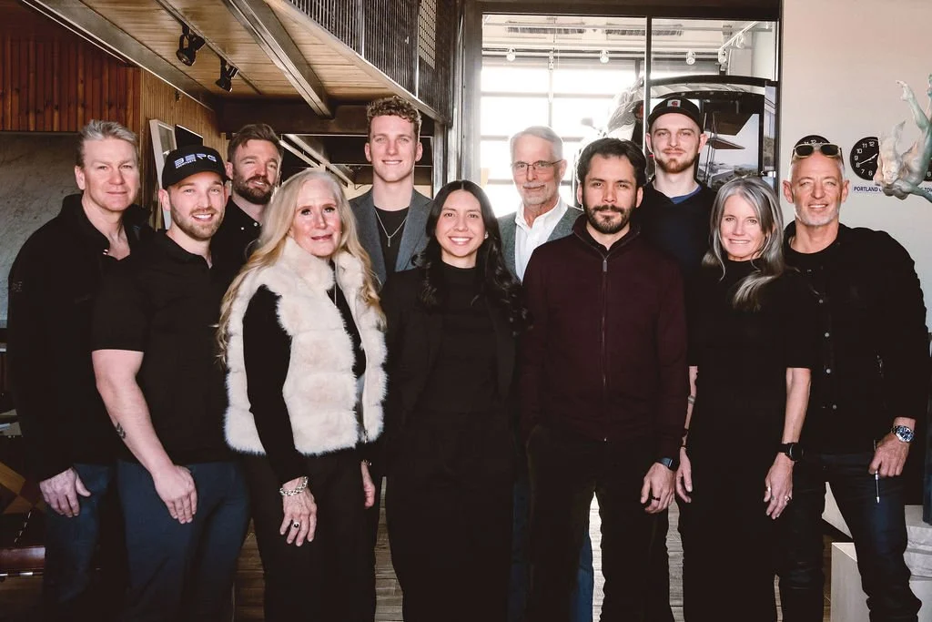 Group of 11 people posing together indoors, dressed in casual to semi-formal attire.