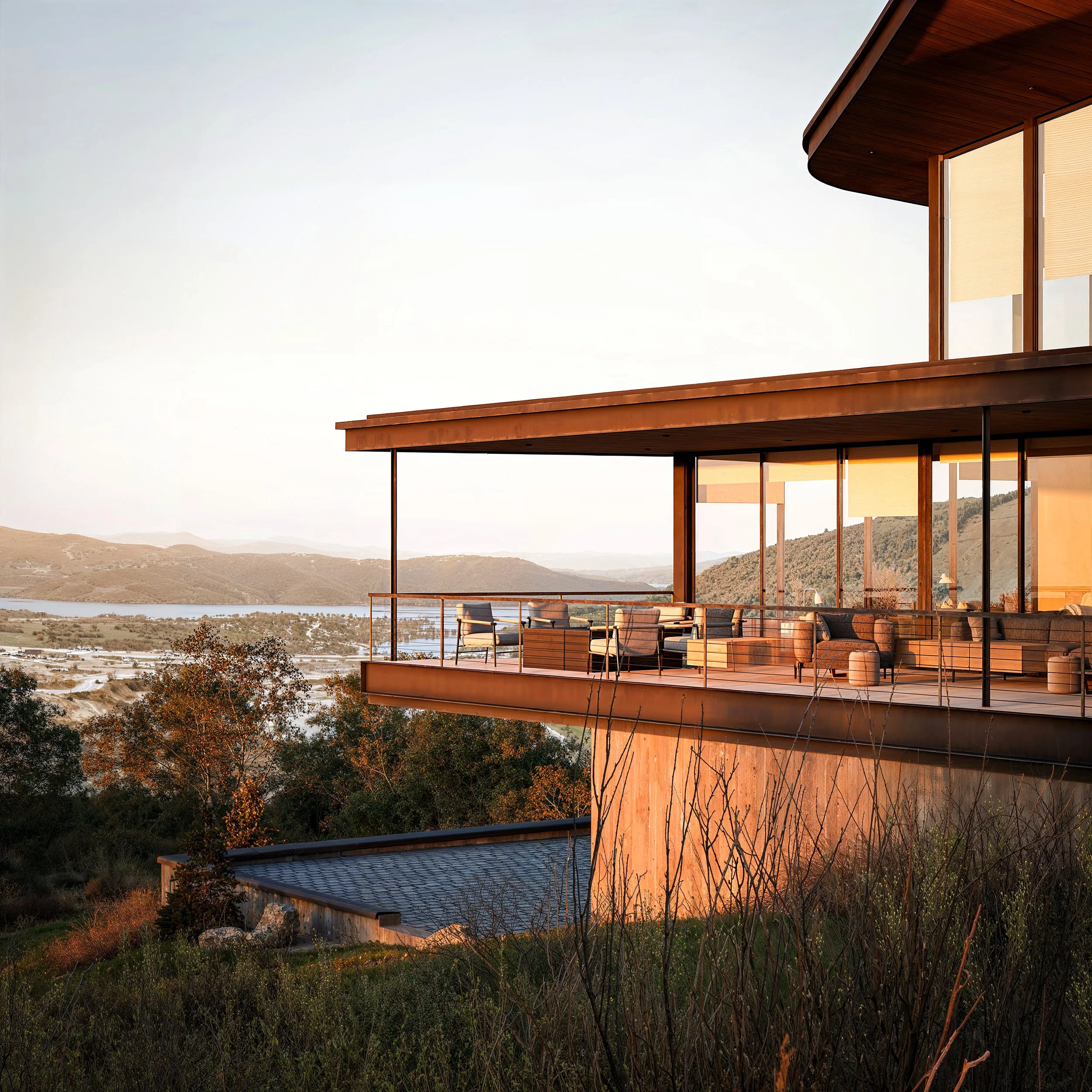 Modern house with floor-to-ceiling windows and a large balcony overlooking a landscape with water and hills in the distance.