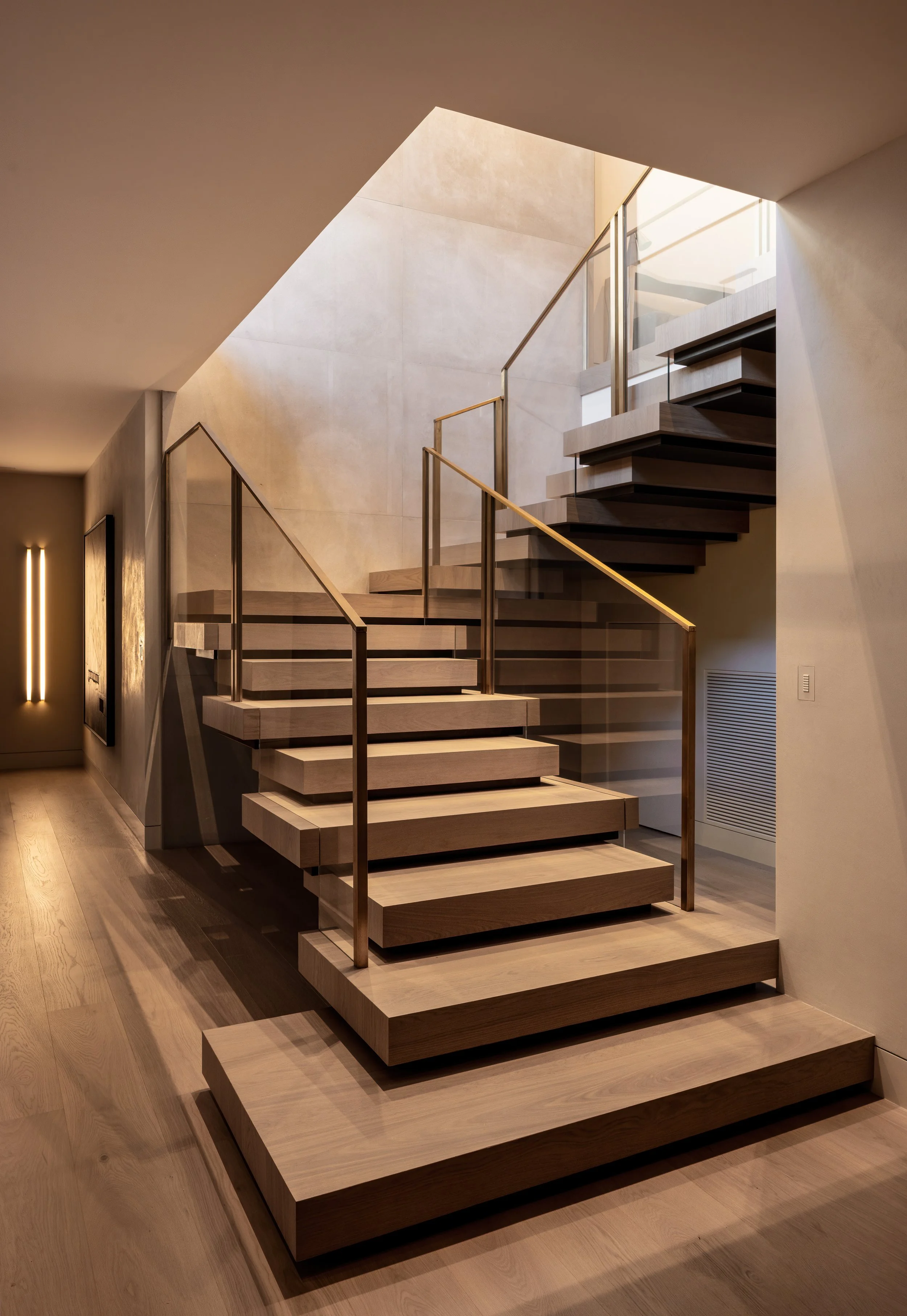 Modern staircase with wide wooden steps, glass railing, and a minimalist design in a spacious, well-lit interior.