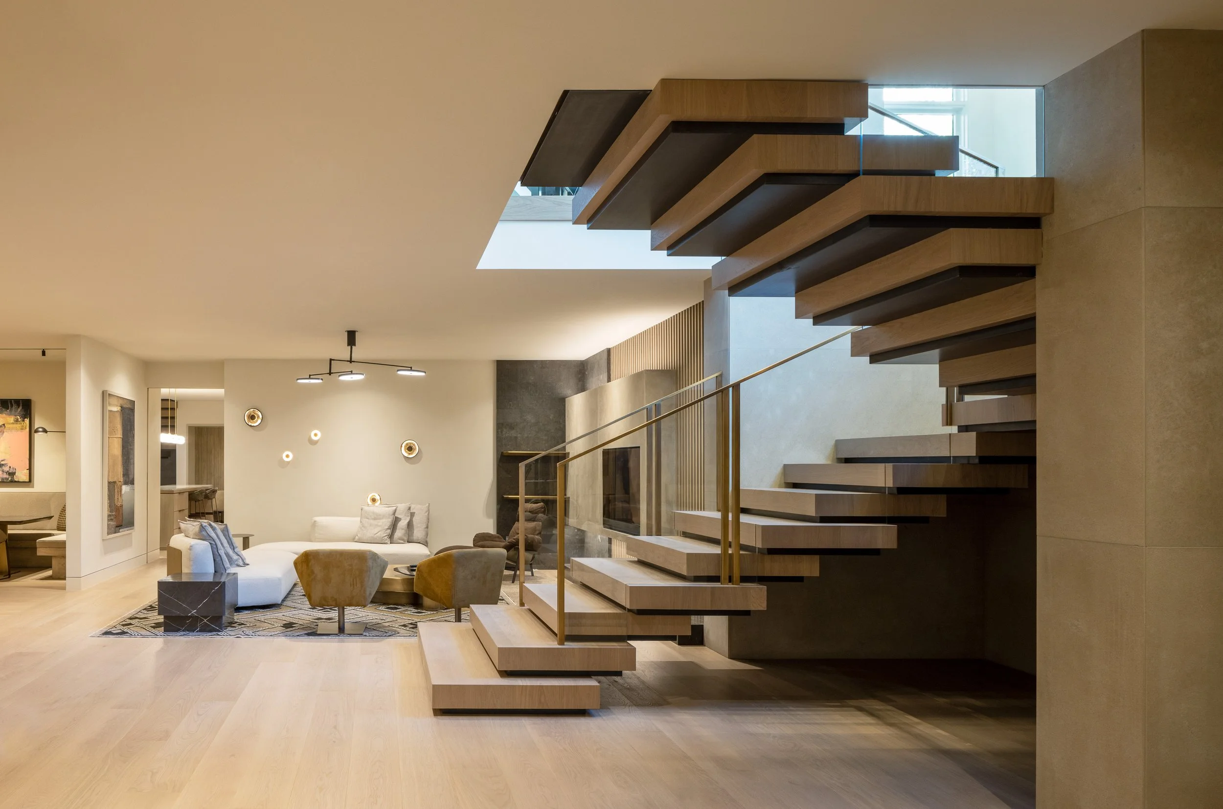Modern living room with a floating wooden staircase, white sofa, armchairs, and wall decor.