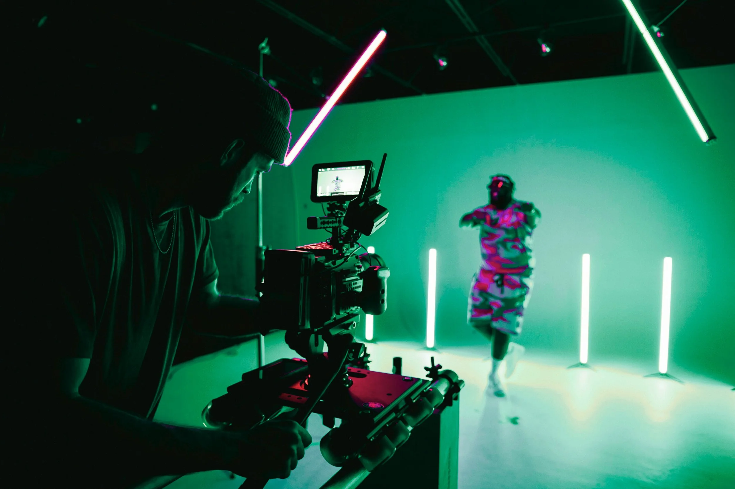 A person filming a dancer in a studio with green and pink neon lights.