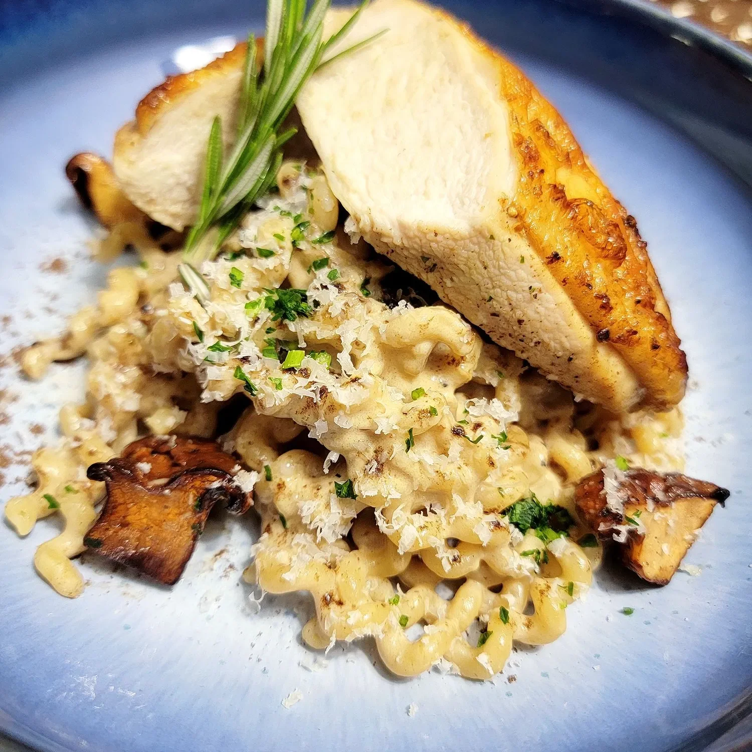 Close-up of a gourmet pasta dish with roasted squash, garnished with herbs and grated cheese, served on a blue plate.