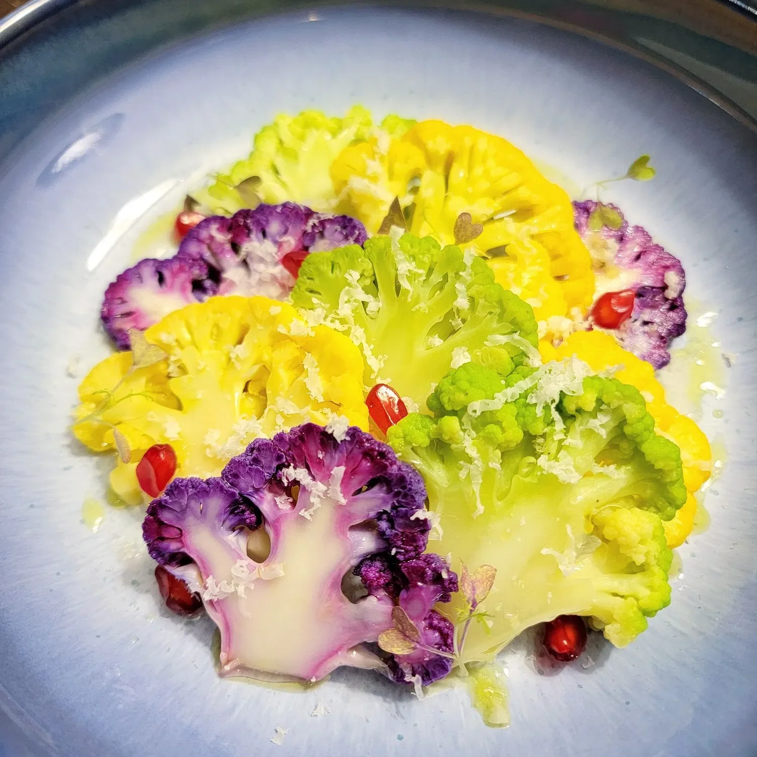Colorful plate of sliced purple, yellow, and green cauliflower with pomegranate seeds and microgreens.