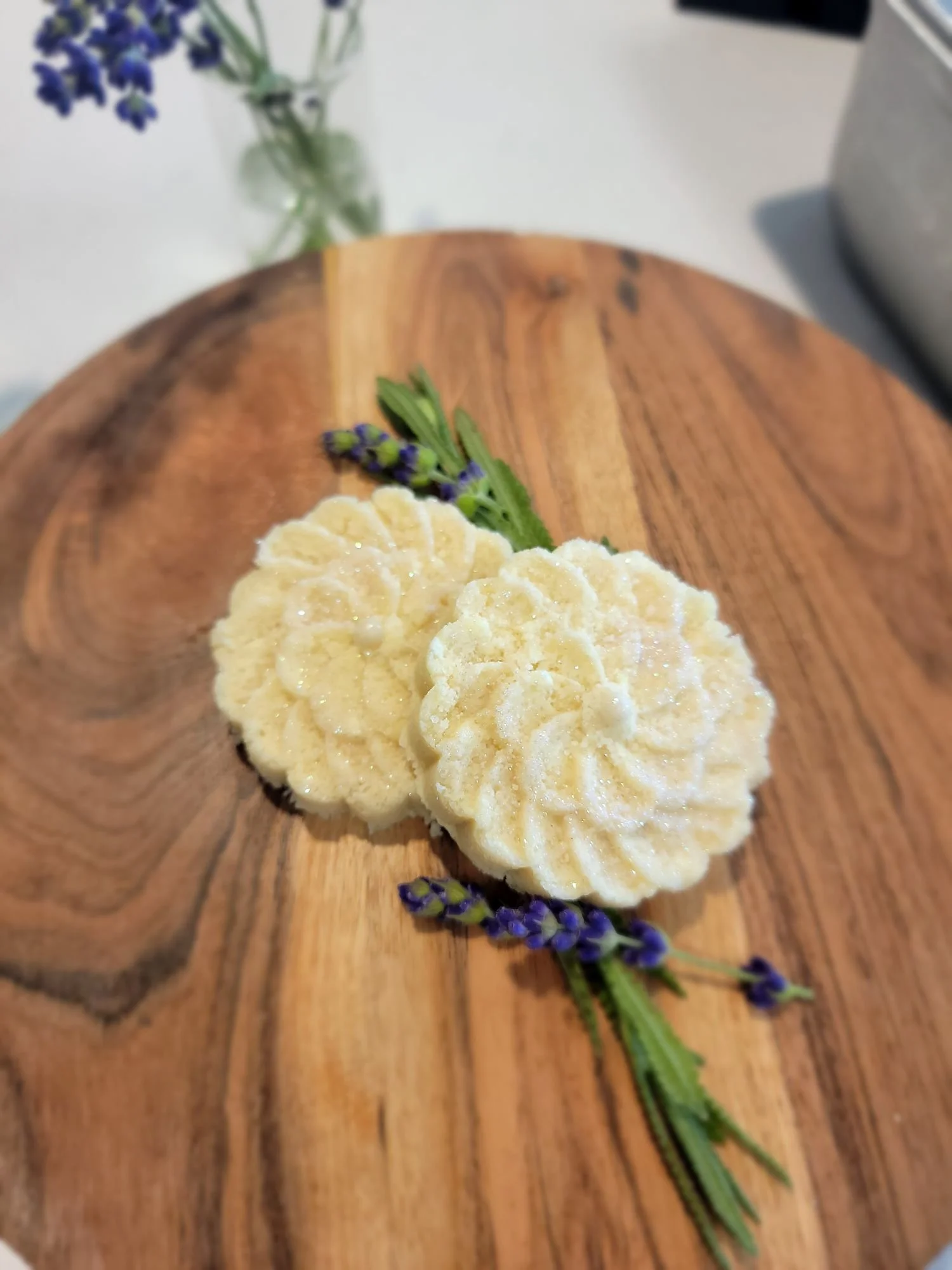 Two cream-colored cookies on a wooden serving board, garnished with sprigs of lavender.
