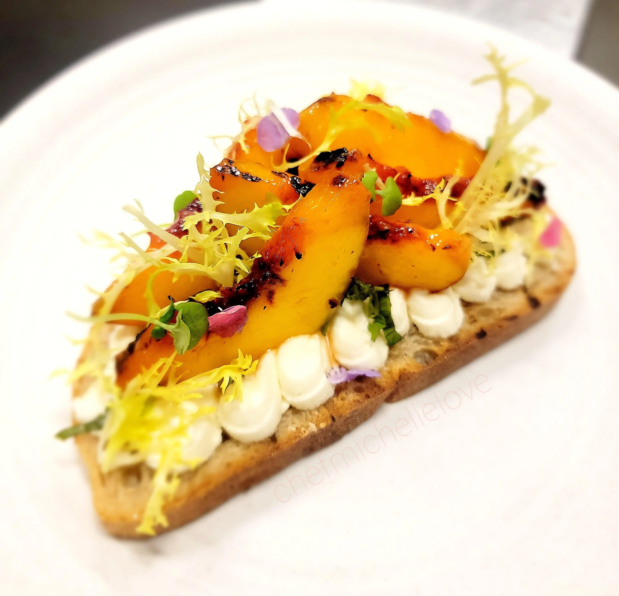 Toast topped with grilled peaches, whipped cream, microgreens, and edible flowers.