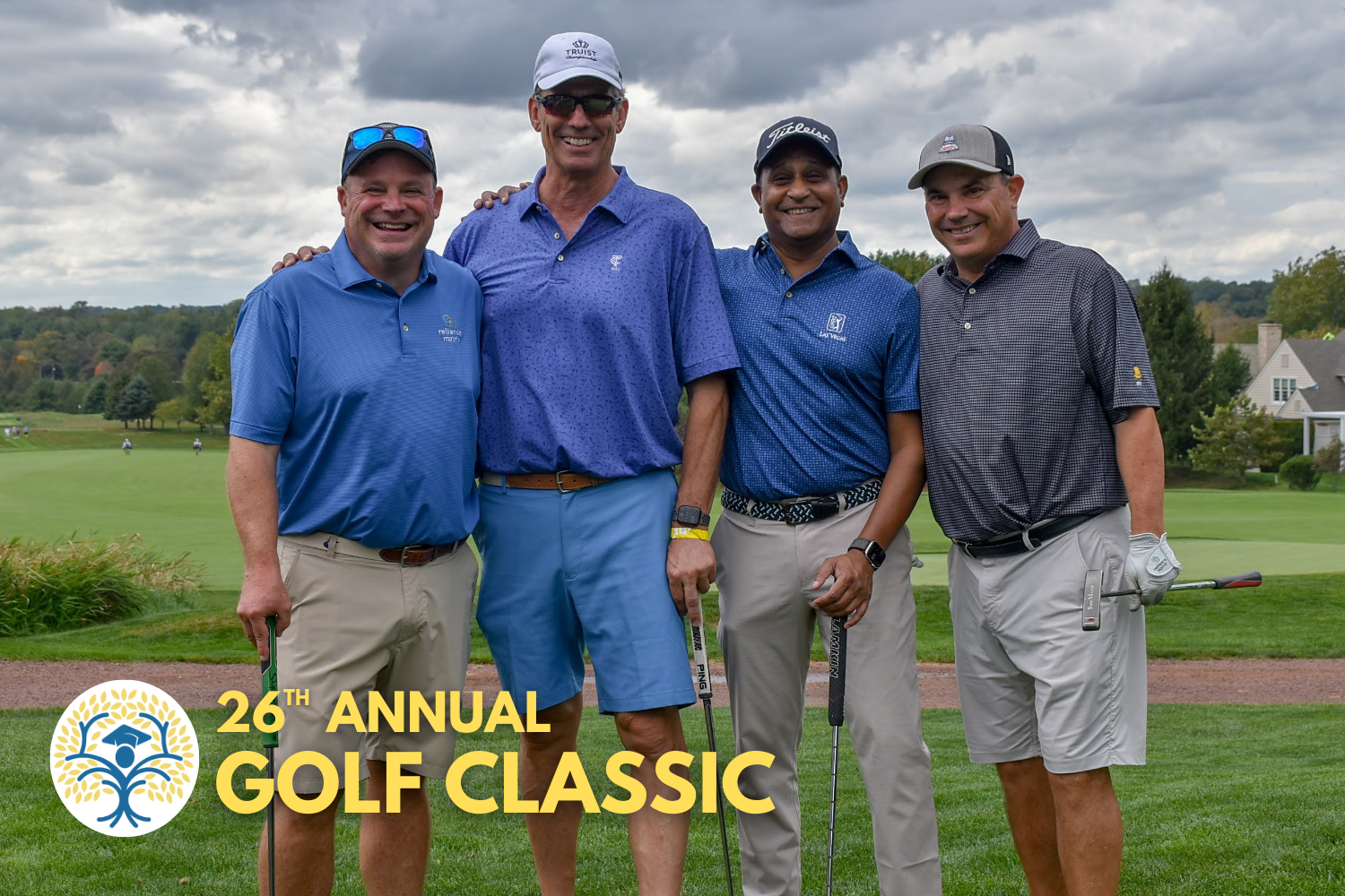Four men standing together on a golf course, smiling at the camera, at the 26th Annual Golf Classic event, with trees and houses in the background.