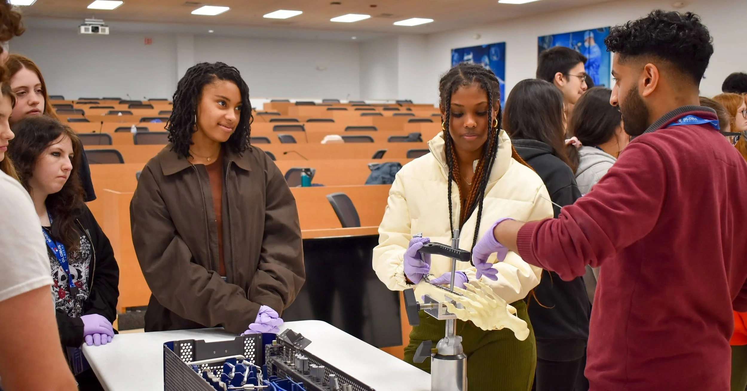 A group of students and a male instructor with gloves, viewing a human pelvis model during a hands-on educational session in a lecture hall.