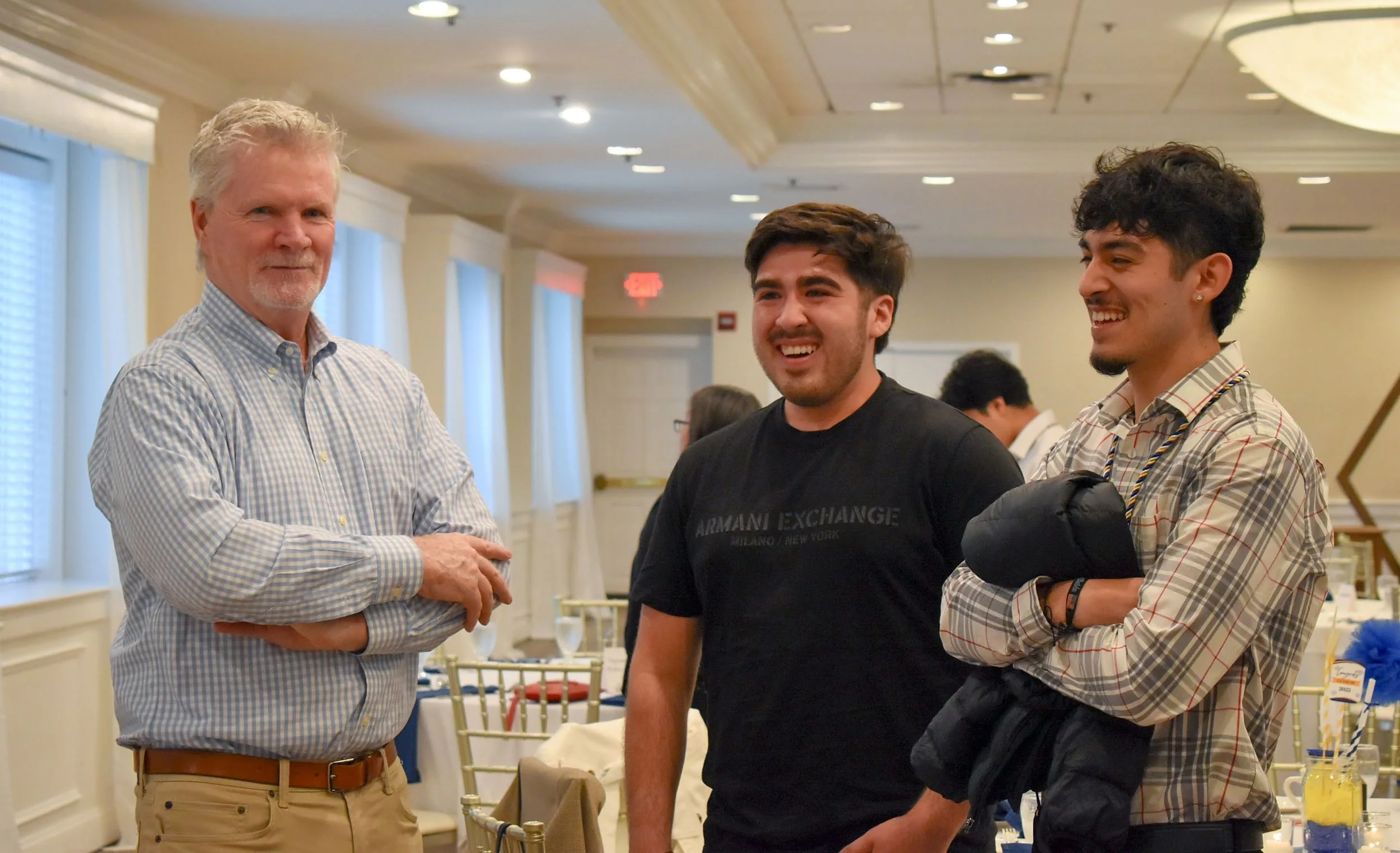Three men standing and talking in a banquet hall, smiling and engaged in conversation.