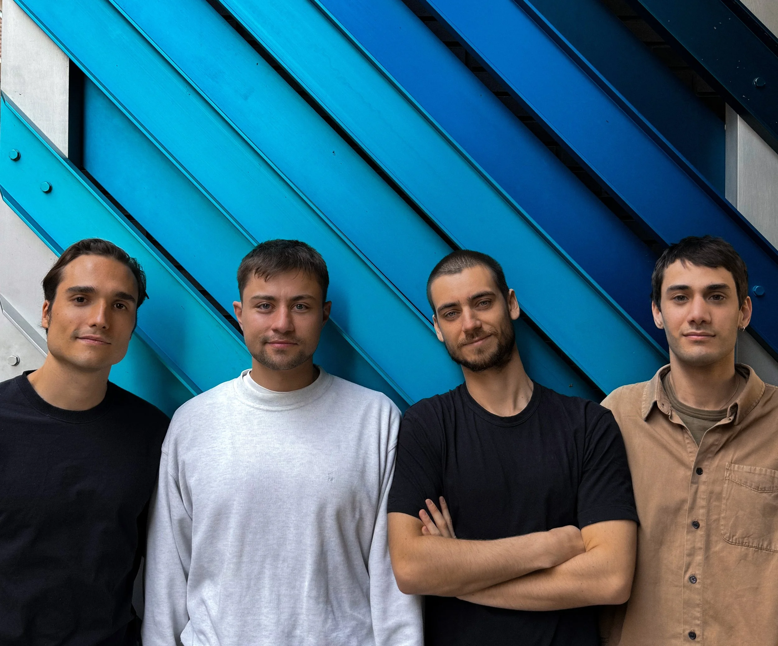 Four men standing shoulder to shoulder in front of a modern geometric blue wall, smiling softly.