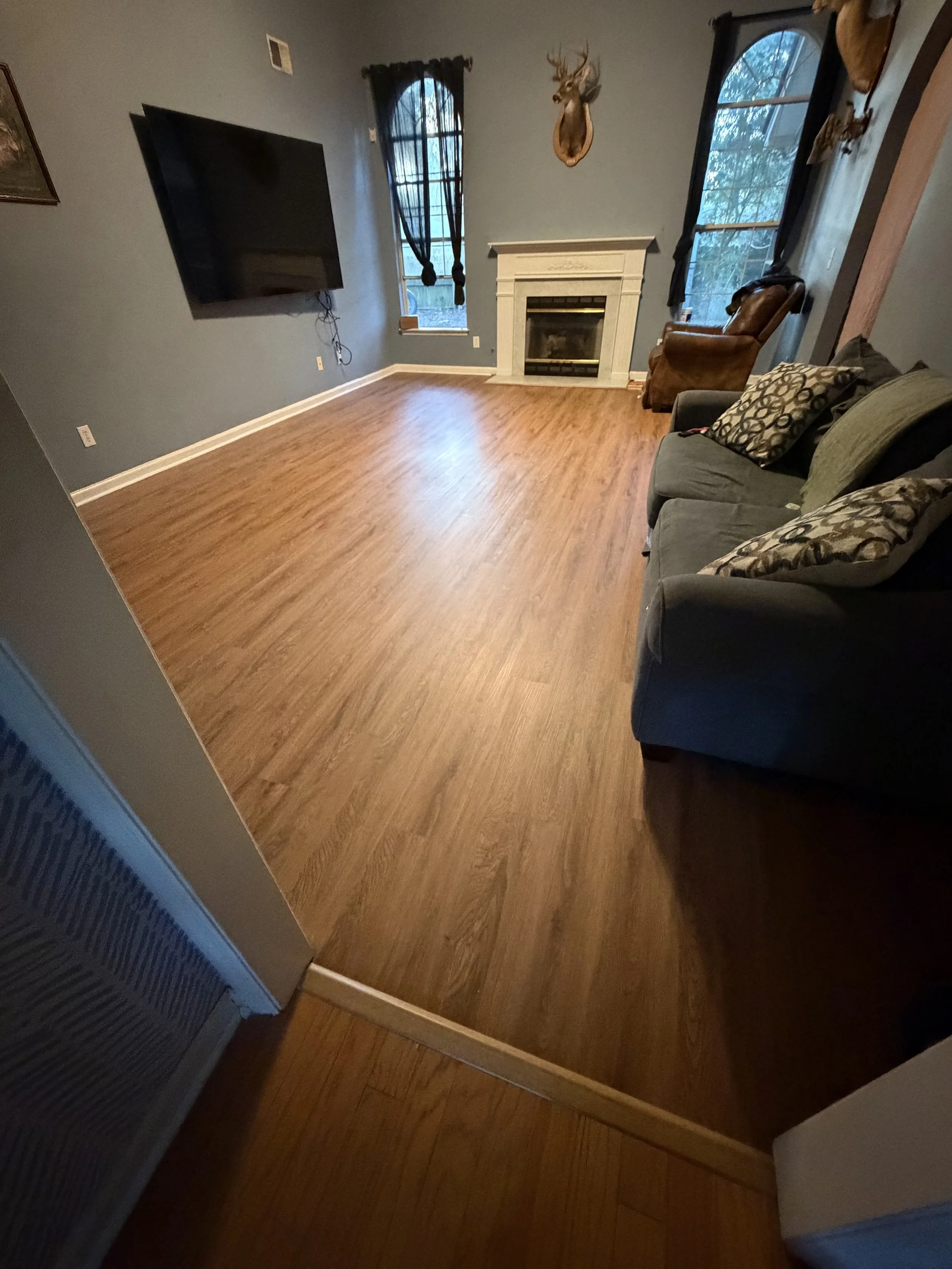 Living room with hardwood floors, a wall-mounted flat-screen TV, a fireplace, and decor including mounted deer heads and a leather chair.