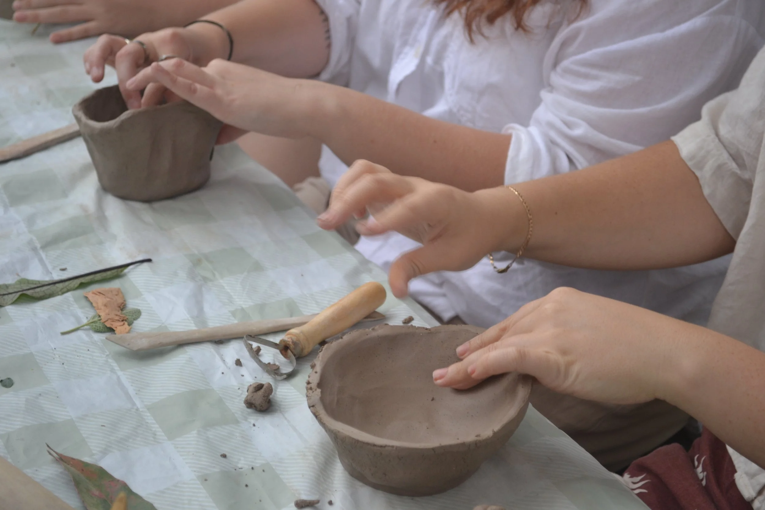 People making pottery with clay on a table, using their hands and tools.