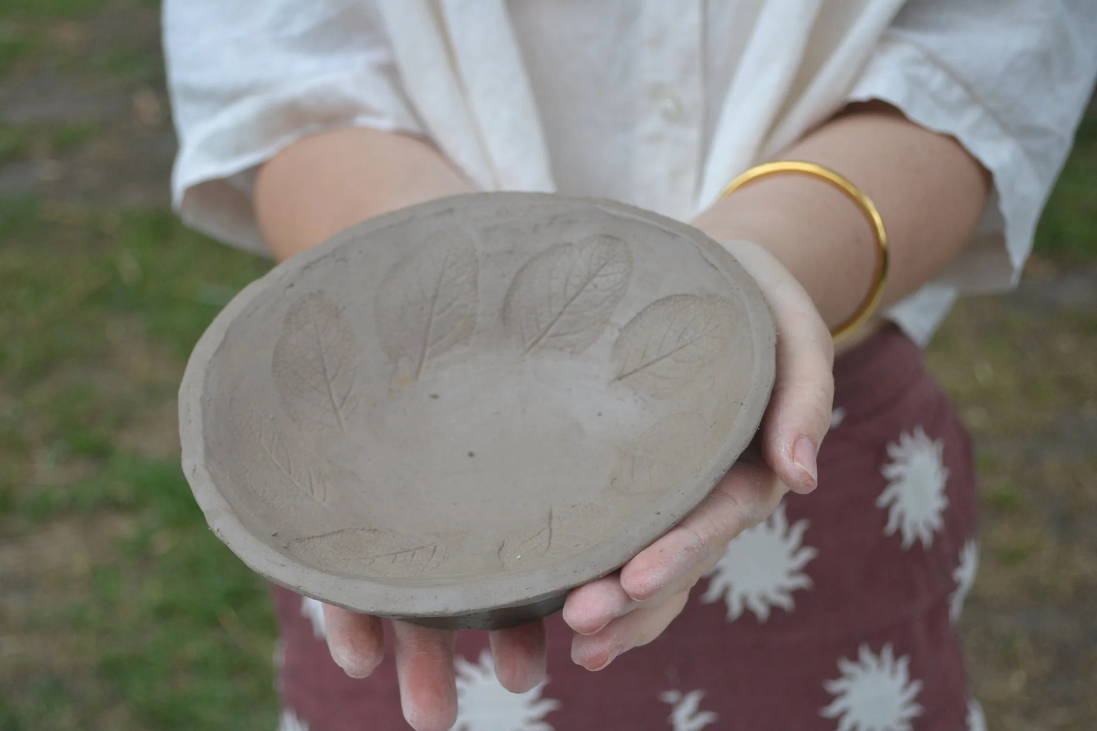 Person holding a decorated hand-built ceramic bowl with leaf imprints