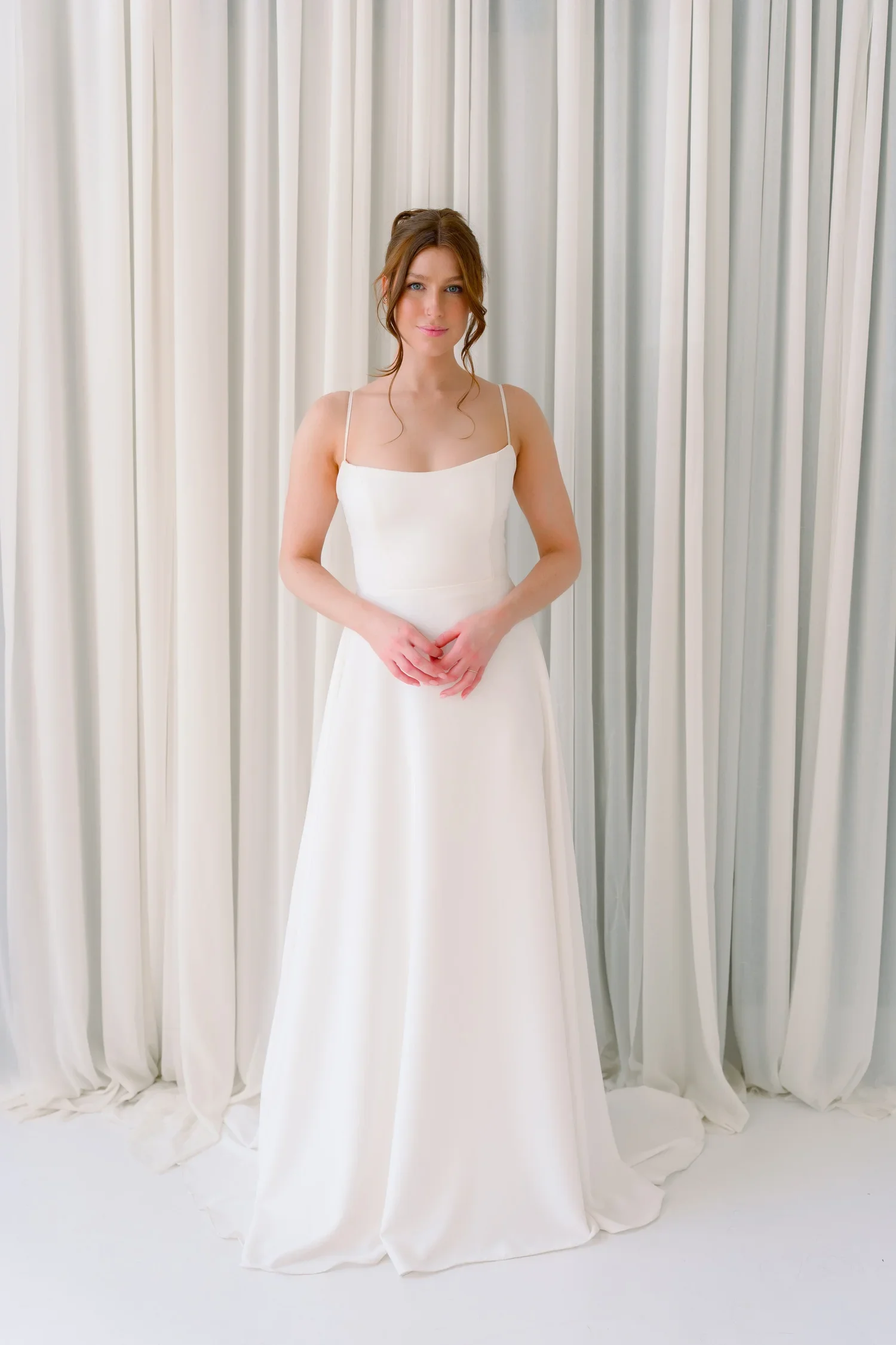 Woman in a white wedding dress standing in front of cream-colored curtains.