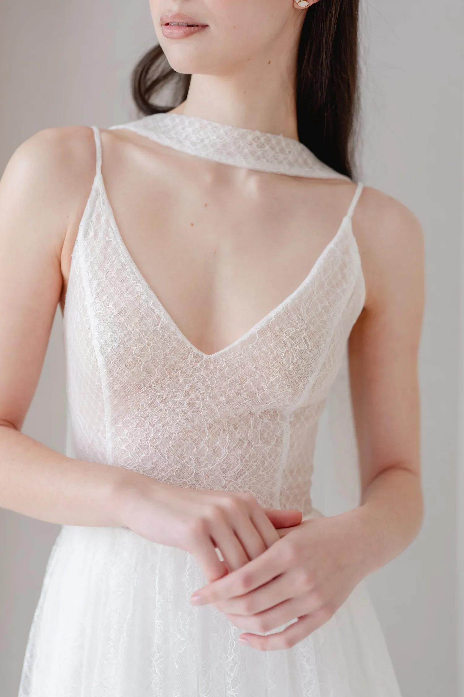 Close-up of a woman in a white lace sleeveless dress, showing her neck and lower face, with her arms crossed in front of her.