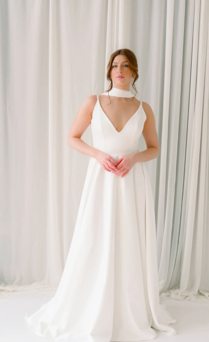 A woman in a white wedding dress standing in front of white curtains.
