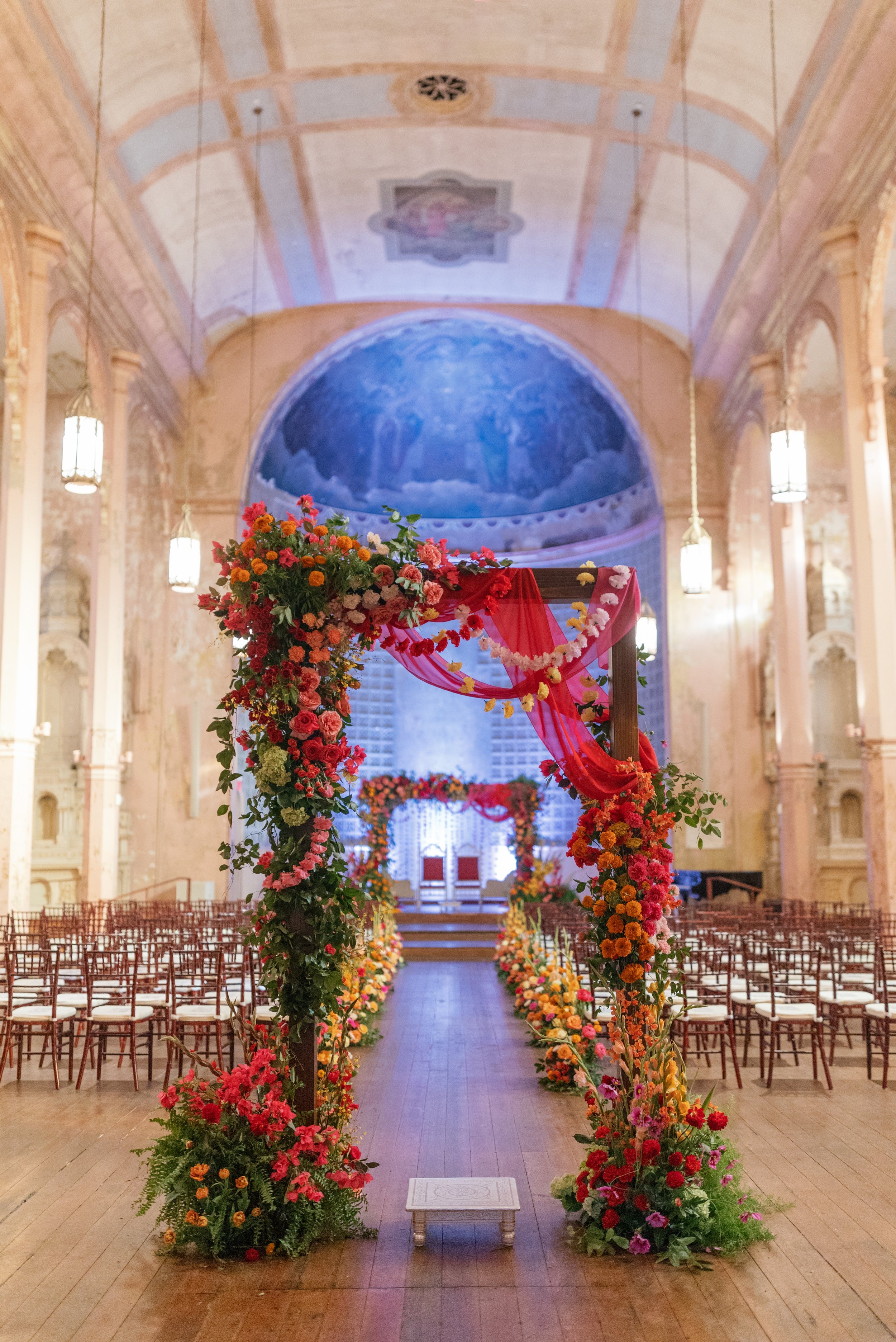 Large floral installation archway framing the aisle and leading to a ceremony stage with a lush vibrant flower covered chuppah at Hotel Peter and Paul in the Bywater, New Orleans.