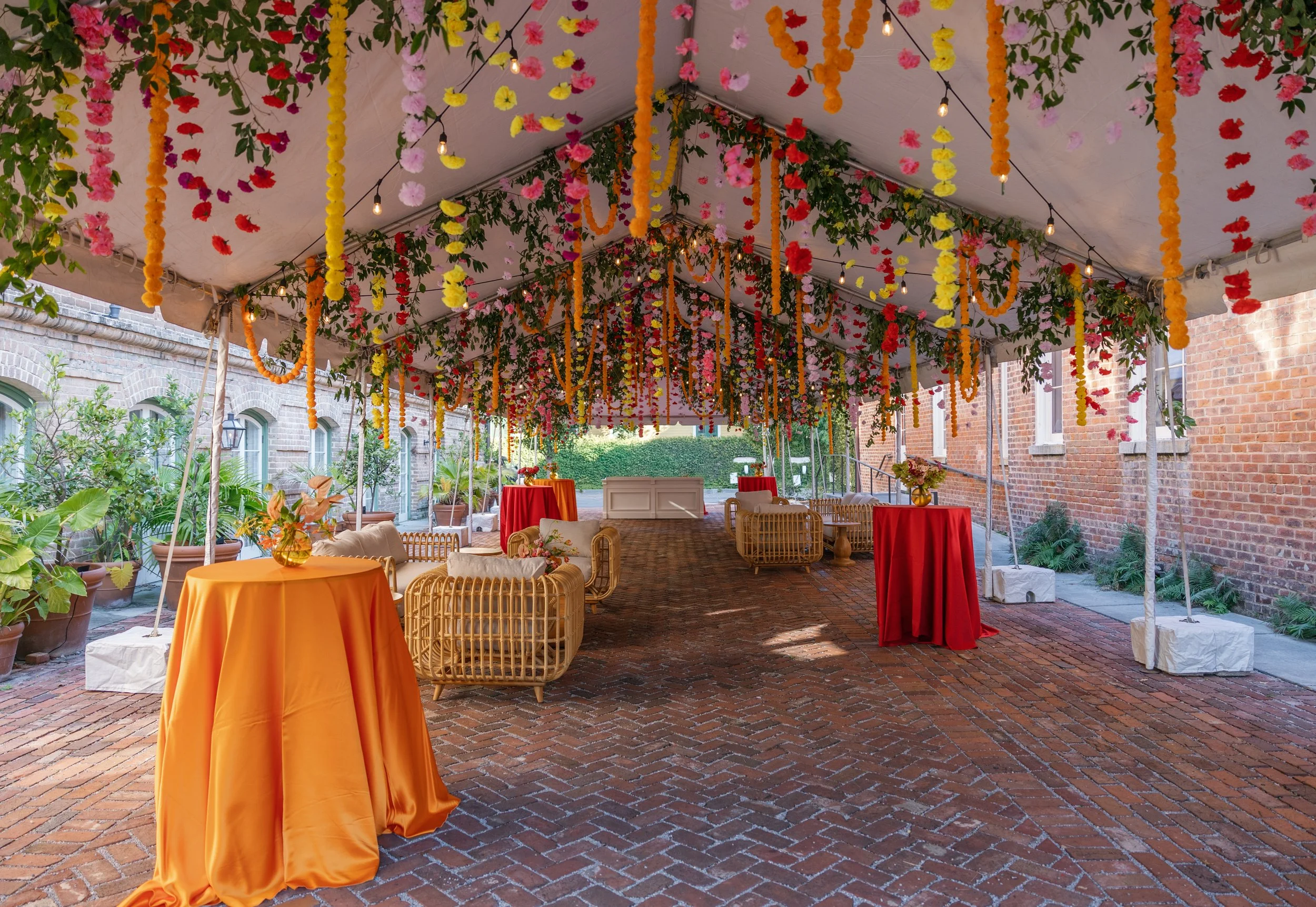 Vibrant colorful hanging carnation installation with greenery over a tented courtyard featuring lounge spaces and bar areas at Hotel Peter and Paul in the ByWater New Orleans.