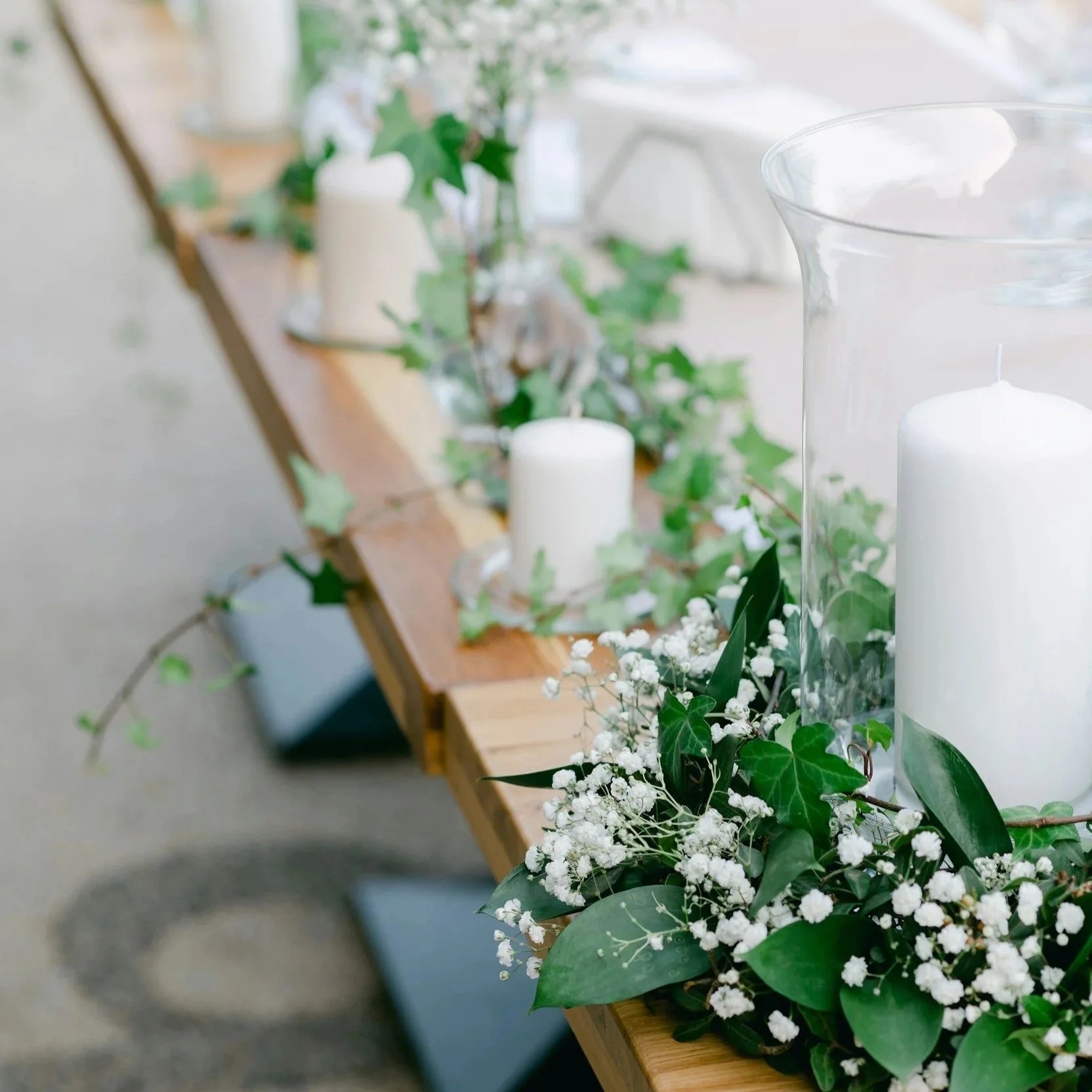 Decorative table with white candles, green leaves, and baby's breath flowers.