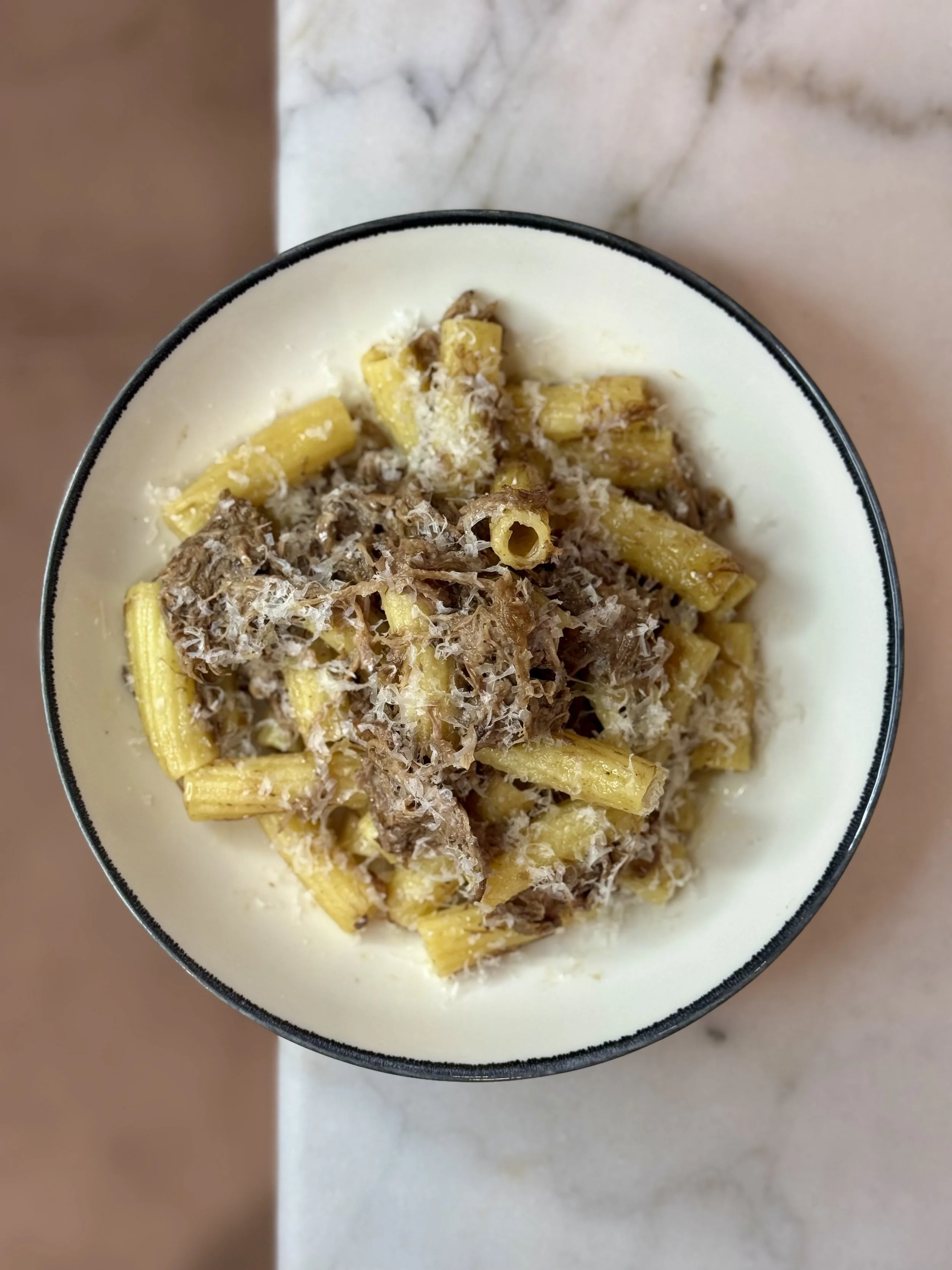 A bowl of cooked pasta topped with grated cheese and shredded meat.