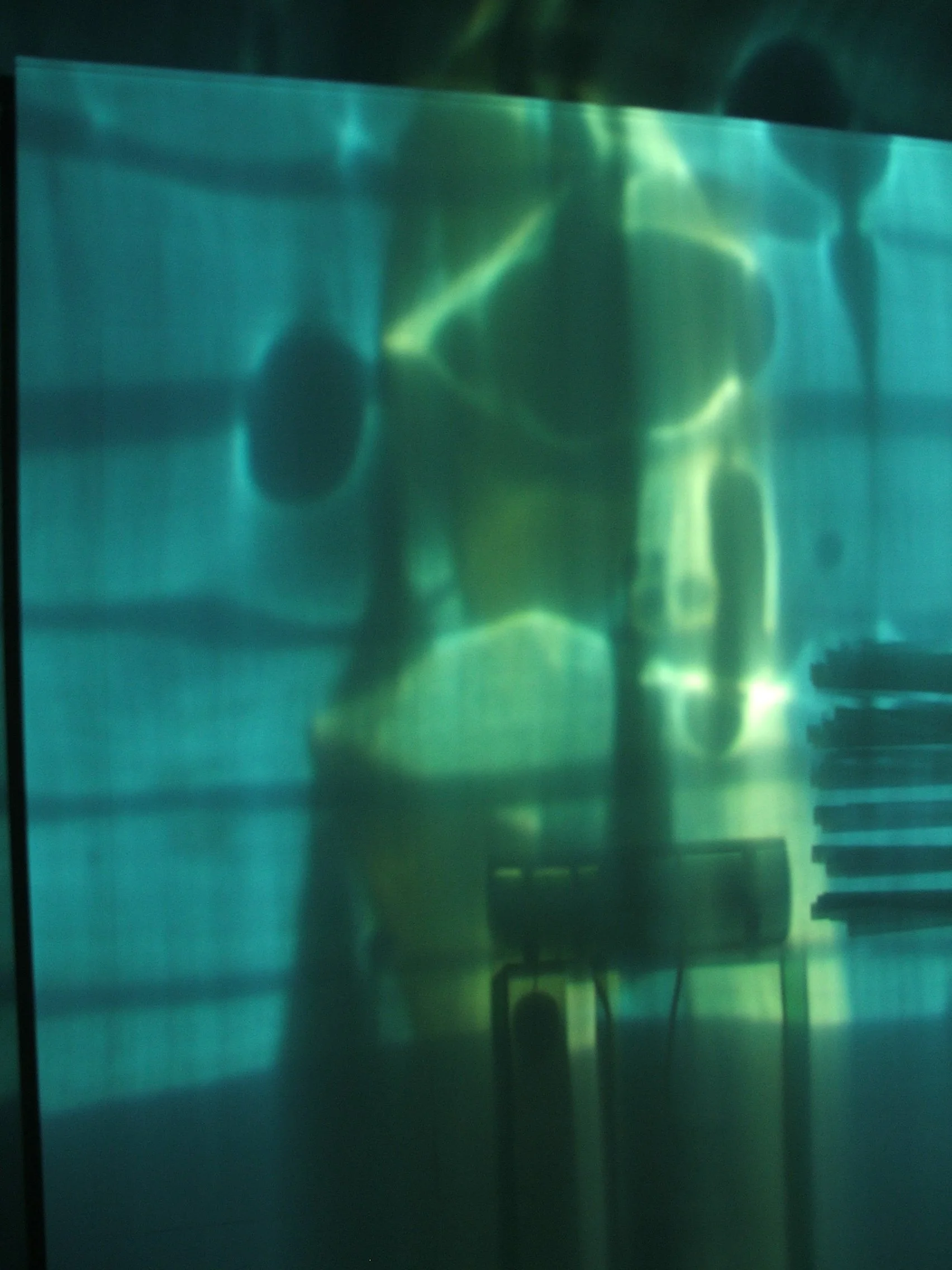 Blurred image of an underwater scene with a person diving or swimming, with greenish-blue hues and indistinct shapes.