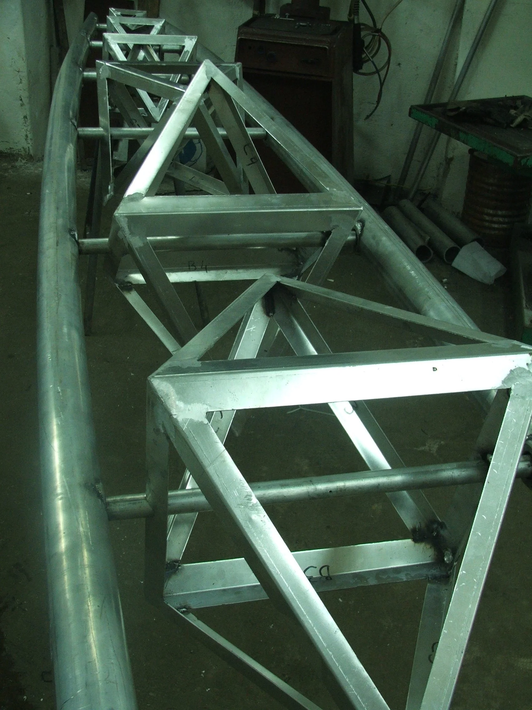 Metal framework structure, possibly part of a construction project or equipment, is placed on the ground in an industrial workshop.