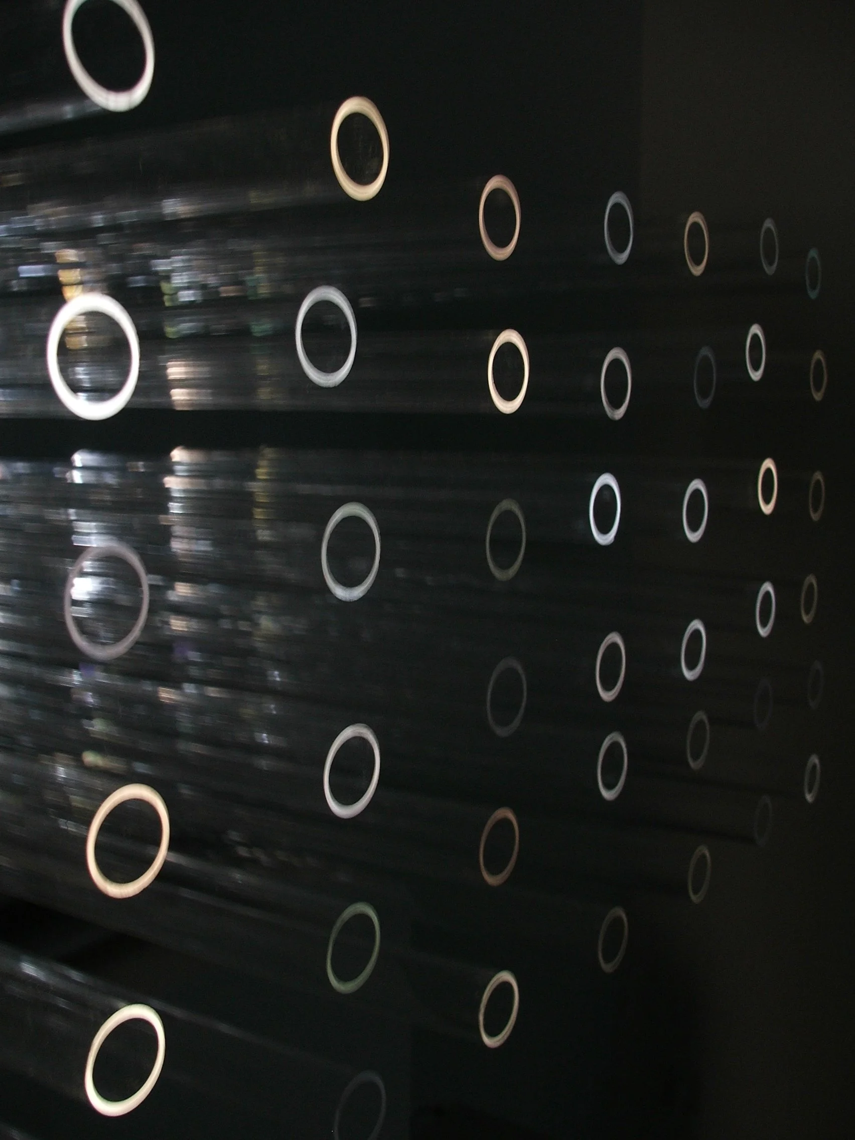 Close-up of a dark, perforated metal surface with circular holes arranged in a grid pattern, with some light reflections visible.