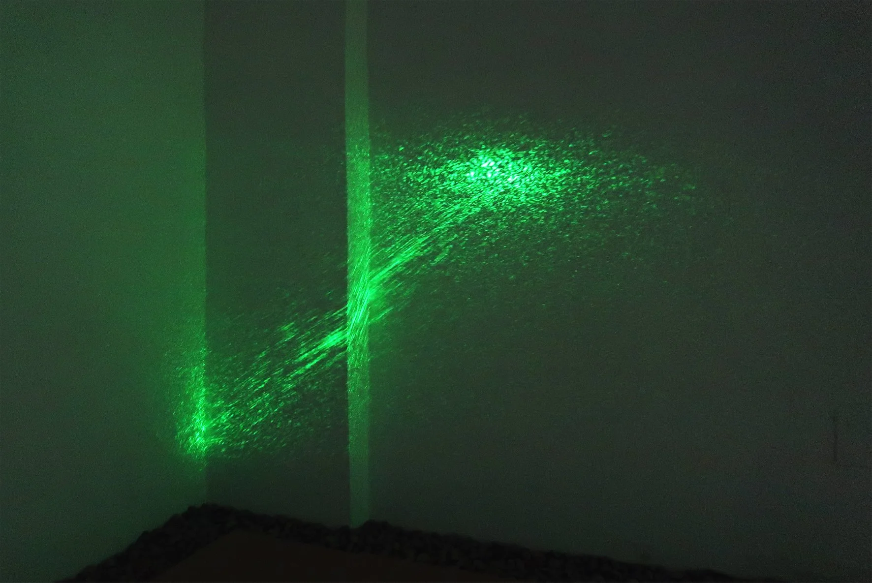Green laser beam projecting a pattern onto a wall in a dark room.