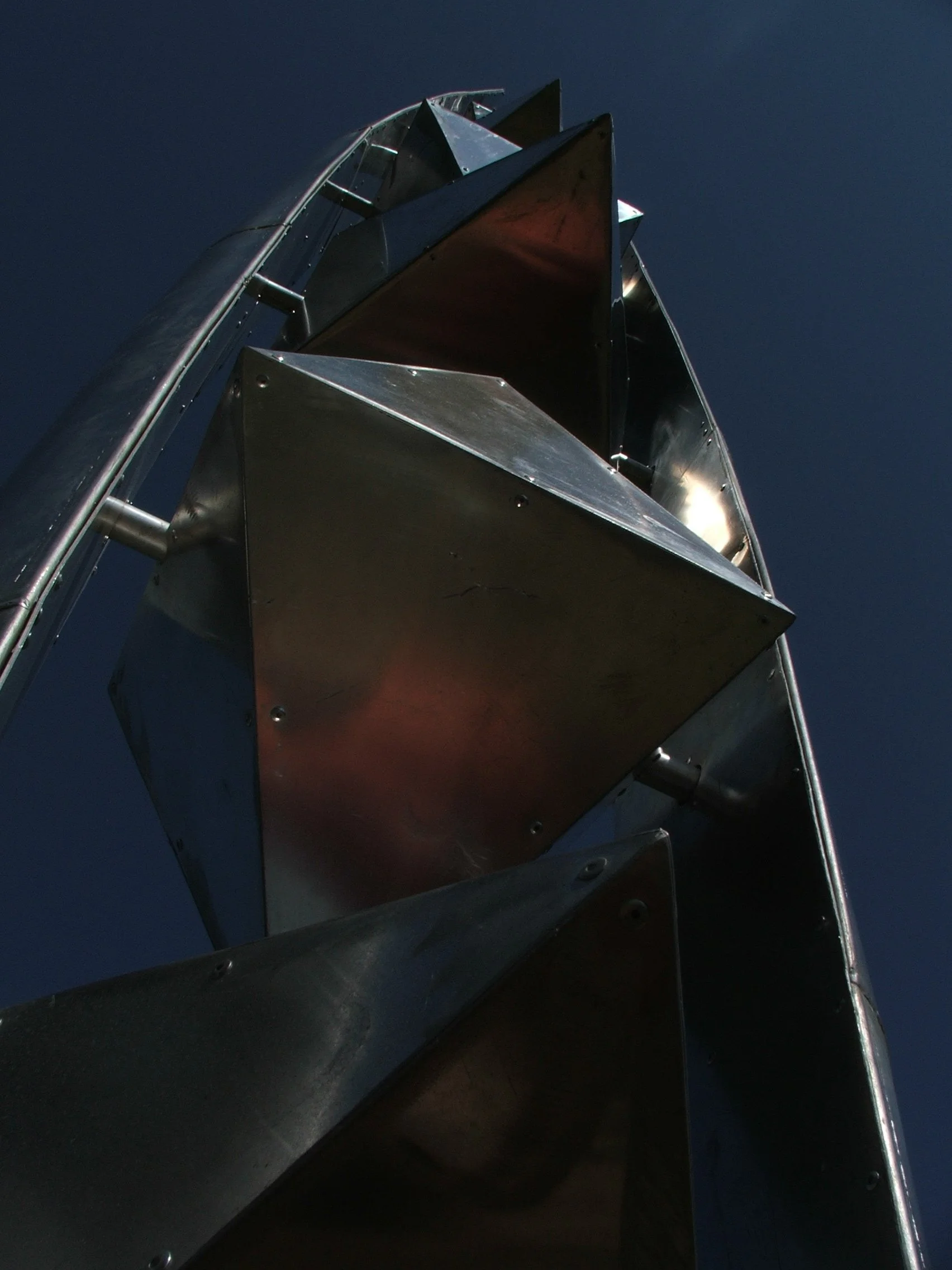 Close-up of a metallic geometric sculpture against a dark blue sky, viewed from below.