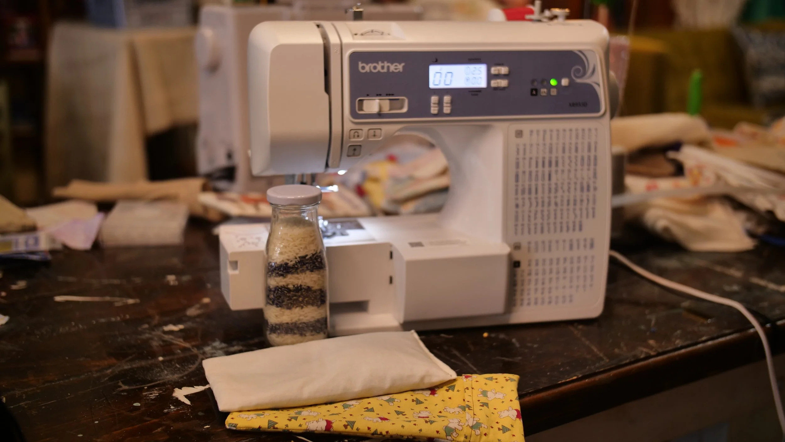 A Brother sewing machine on a cluttered wooden table with fabric and sewing supplies around it.