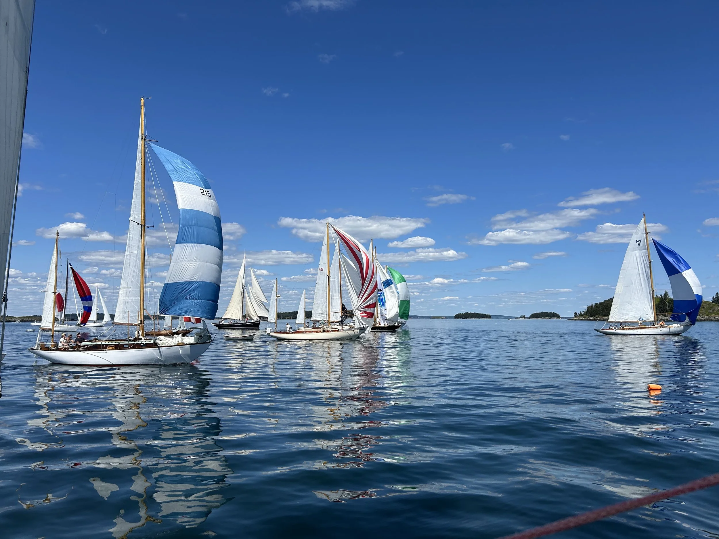 Several sailboats with colorful sails on calm water under a blue sky with scattered clouds.