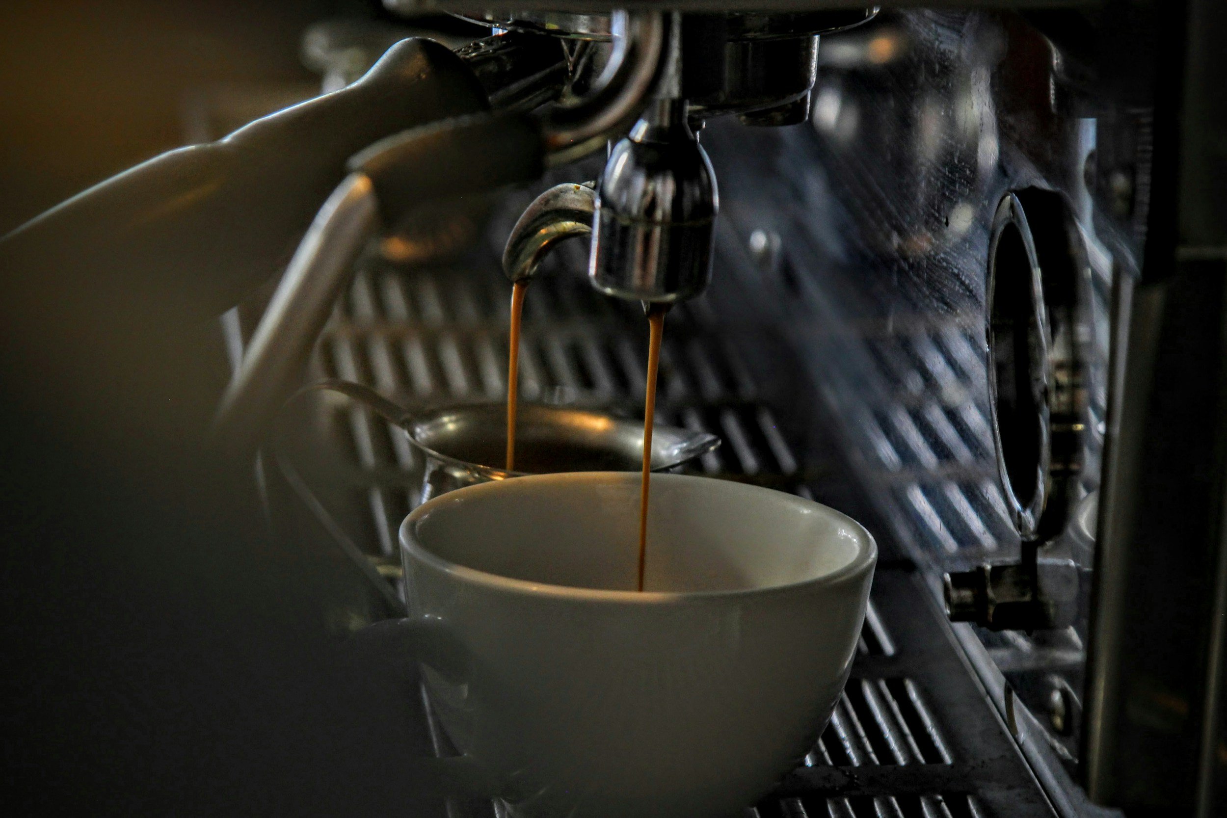 Espresso machine pouring coffee into a white cup, with a small milk frothing pitcher in the background.