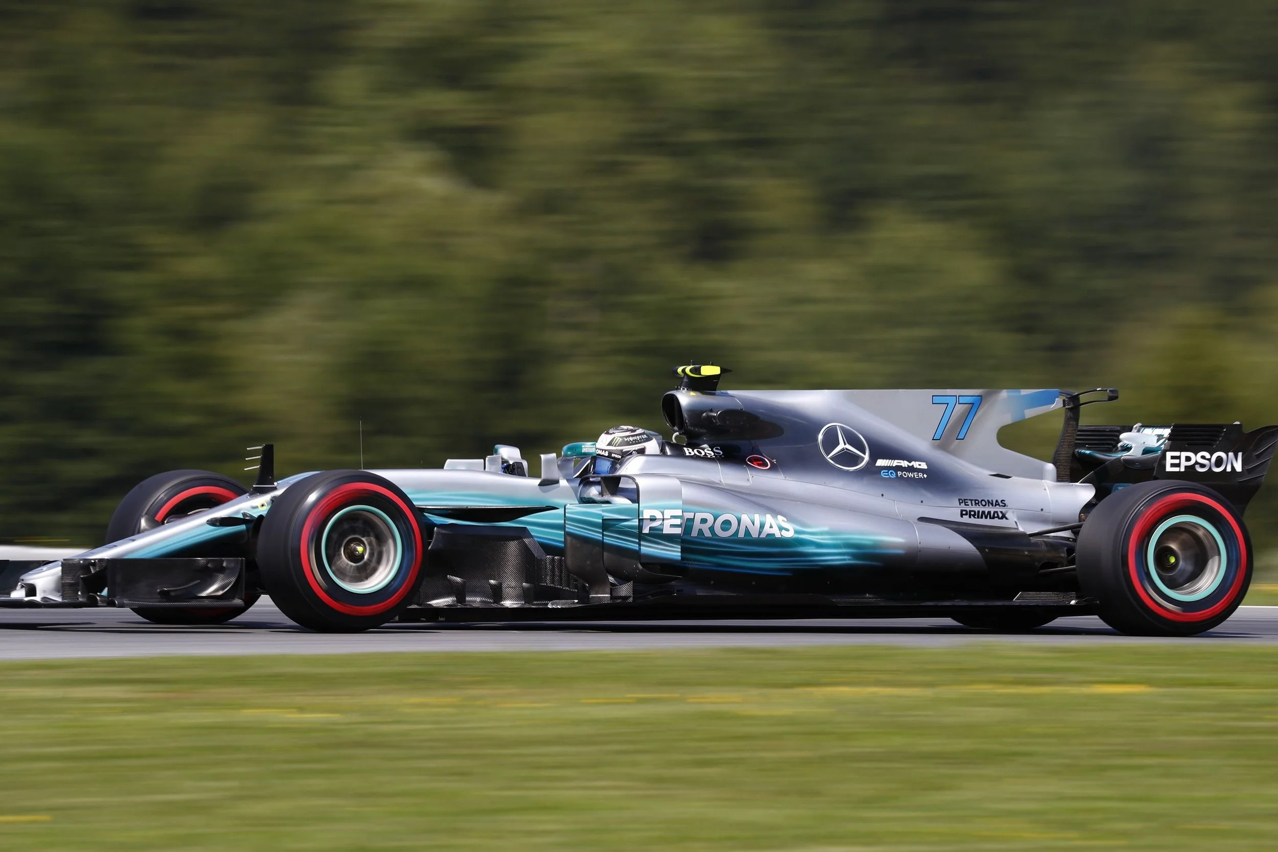 A Mercedes Formula 1 race car speeding on a track with a blurred green background.