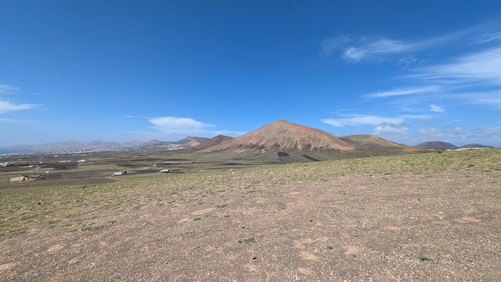 Scenic view of a wide purple, green, and brown volcanic mountain landscape under a blue sky with wispy clouds.