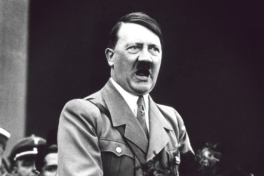 Black-and-white photo of Adolf Hitler speaking passionately, wearing a military uniform, with a serious expression on his face.