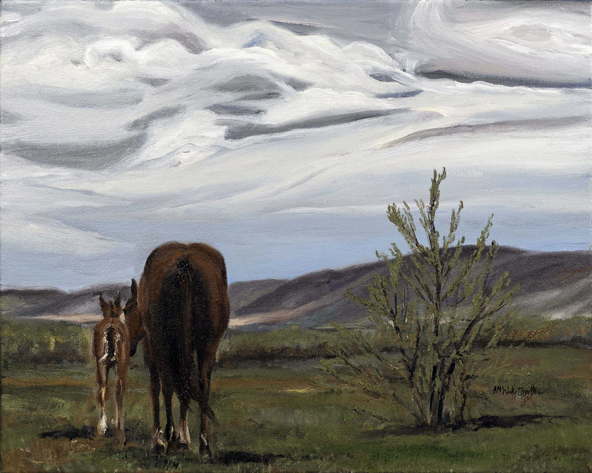 A rural landscape featuring two horses, one adult and one foal, standing on grass near a small tree with hills and cloudy sky in the background.
