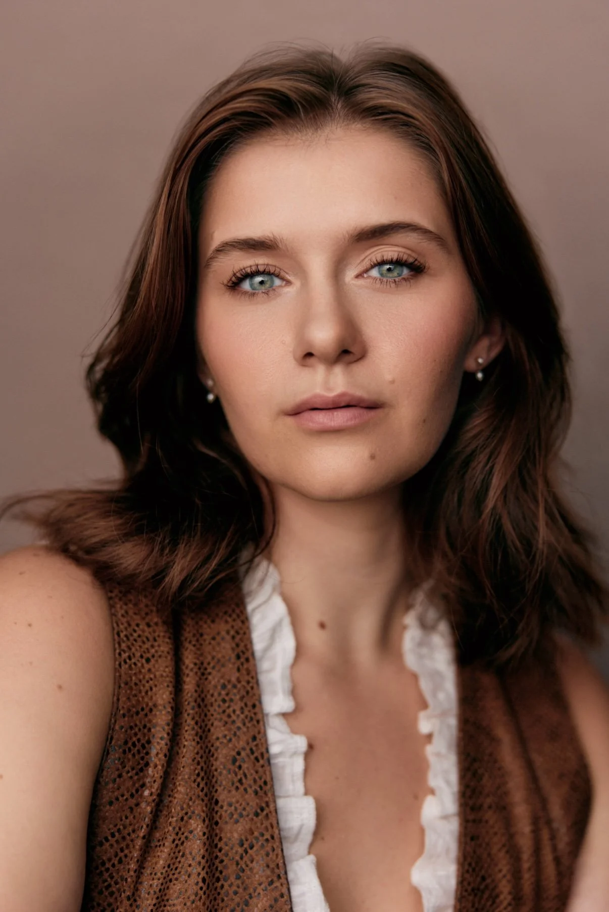 A young woman with wavy brown hair, blue eyes, and light skin, looking directly at the camera with a pensive, warm look. Golden age, intriguing and confident