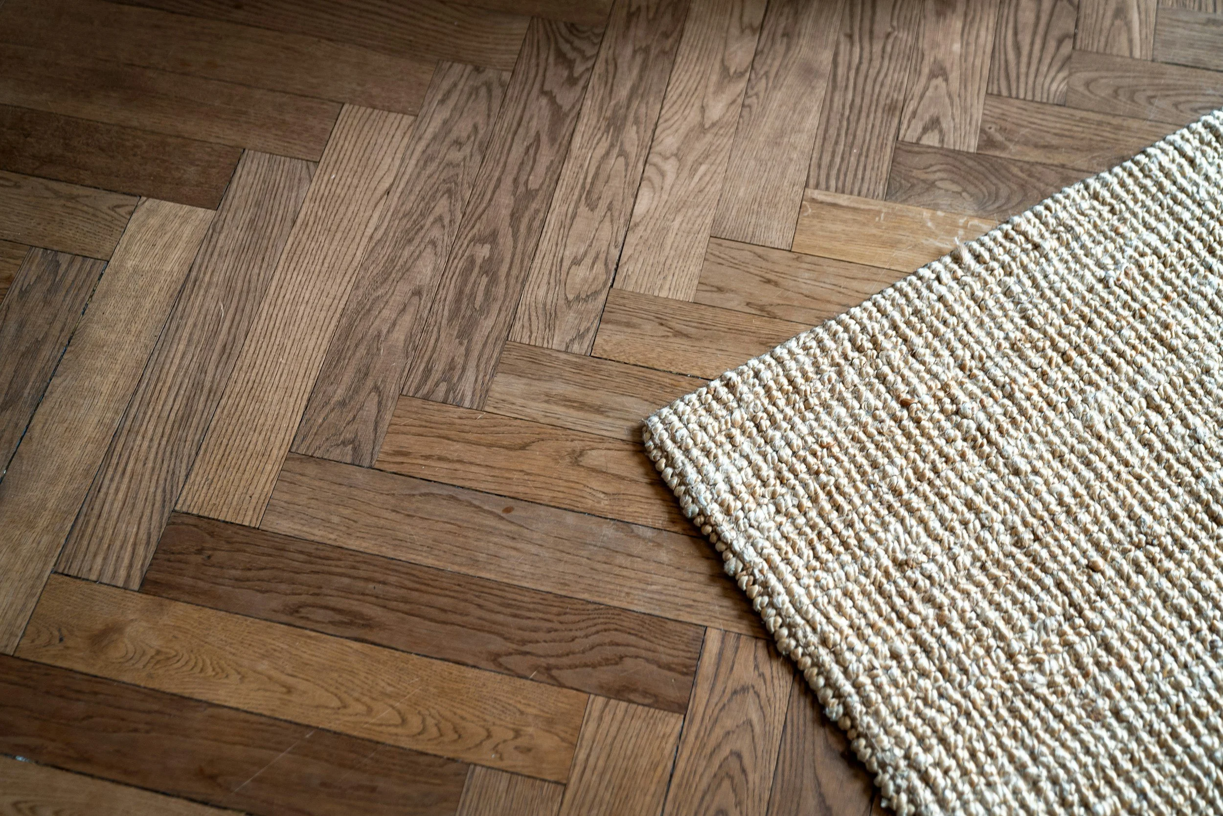 Close-up view of a wooden parquet floor and a corner of a beige textured rug.