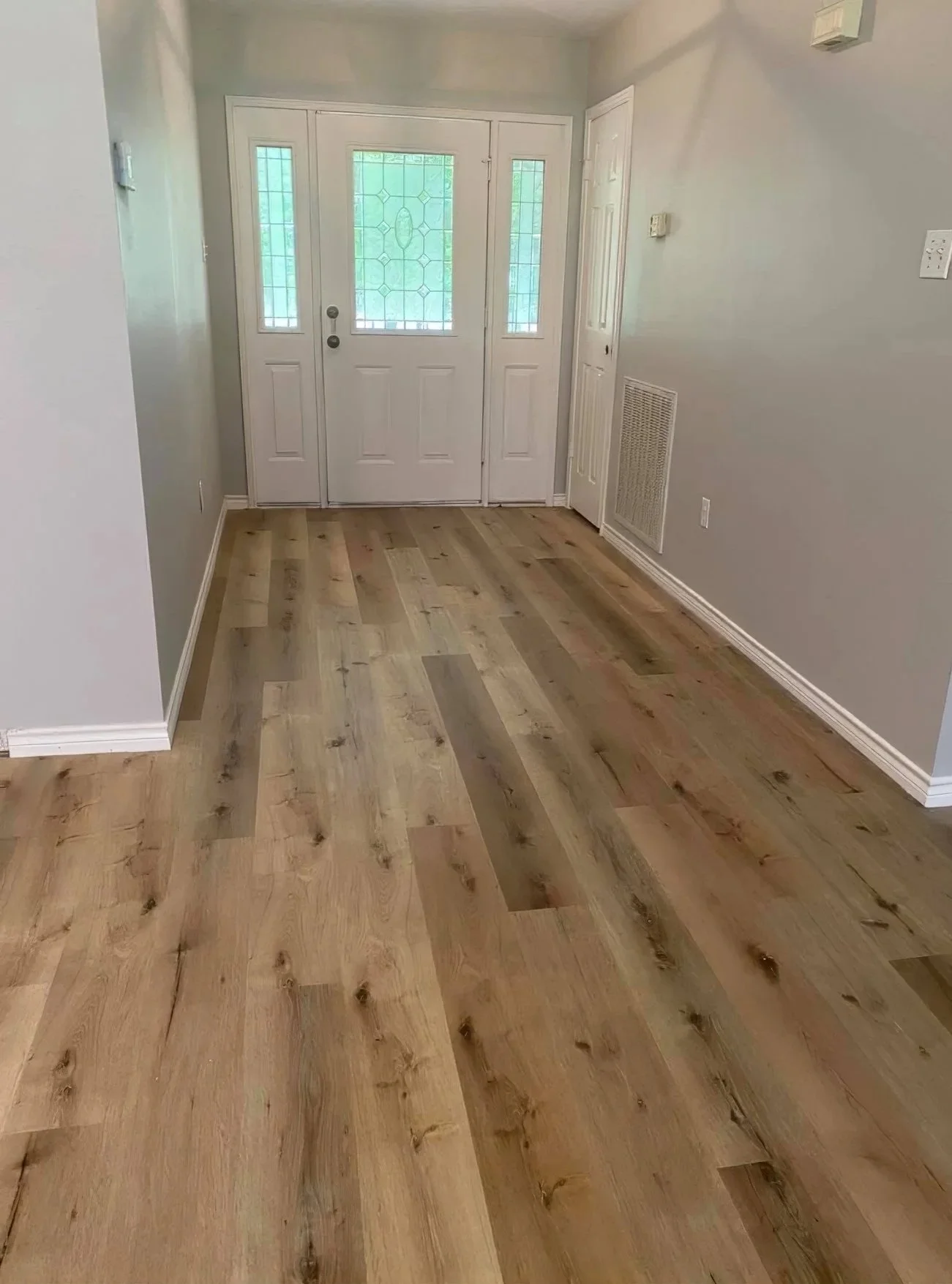 Empty foyer with a wooden floor, front door with decorative glass, and side doors.