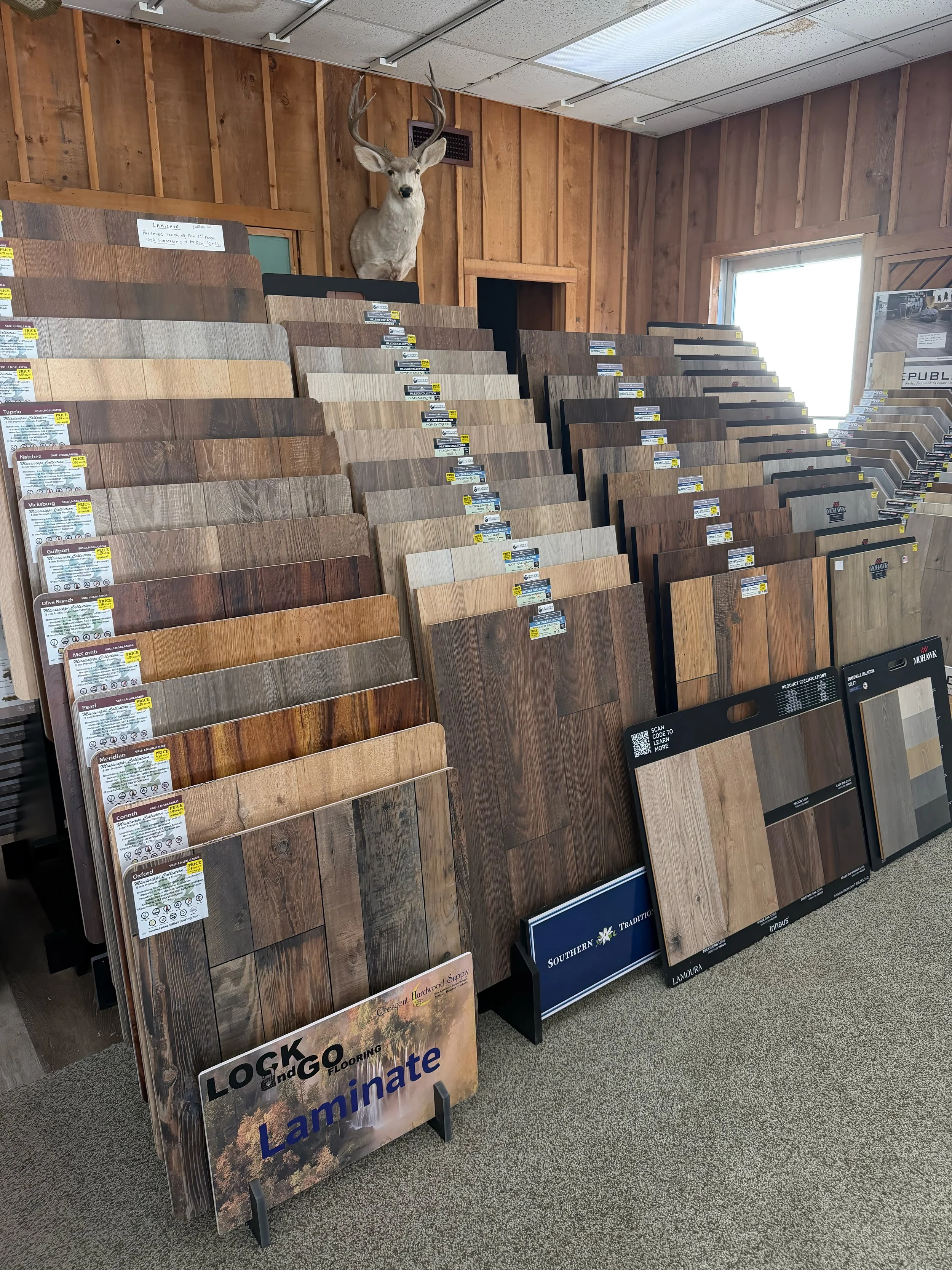Display of various laminate flooring samples arranged in racks, topped with a mounted deer head.