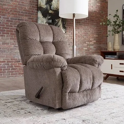 A brown upholstered recliner chair in a living room with a brick wall, a tall white floor lamp, and a white console table with decorative items.