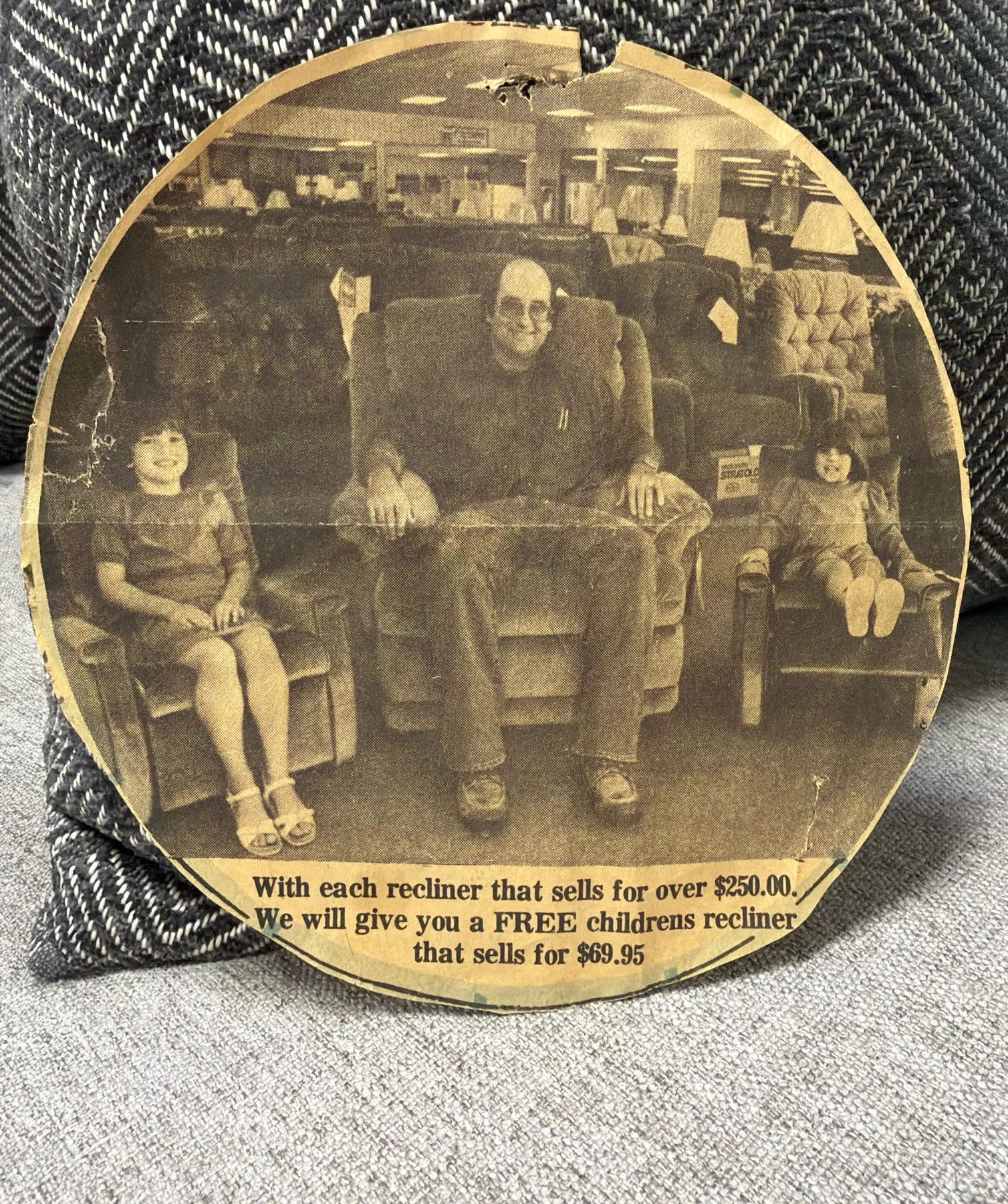 Vintage photo of a man sitting in a recliner flanked by two young girls in chairs, with furniture and lamps in the background. Text at the bottom offers a free children's recliner with the purchase of a reclining chair.