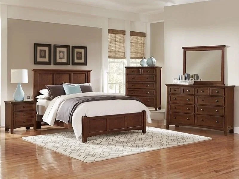 A bedroom with a wooden bed, nightstand, and dresser, decorated with lamps, artwork, and a mirror.