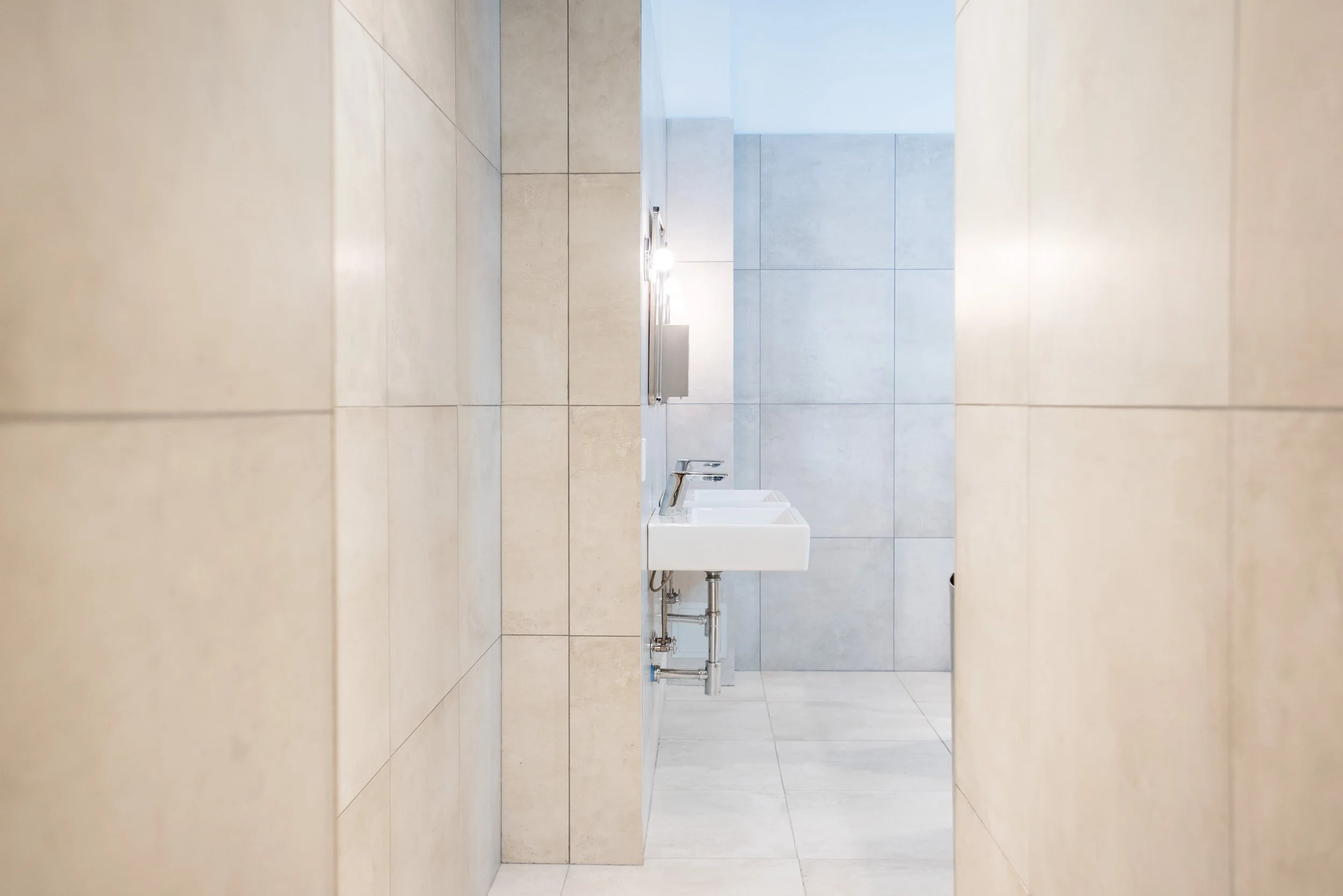 restroom with two sinks and mirrors, beige tiles on walls, and light gray tiles on the floor.