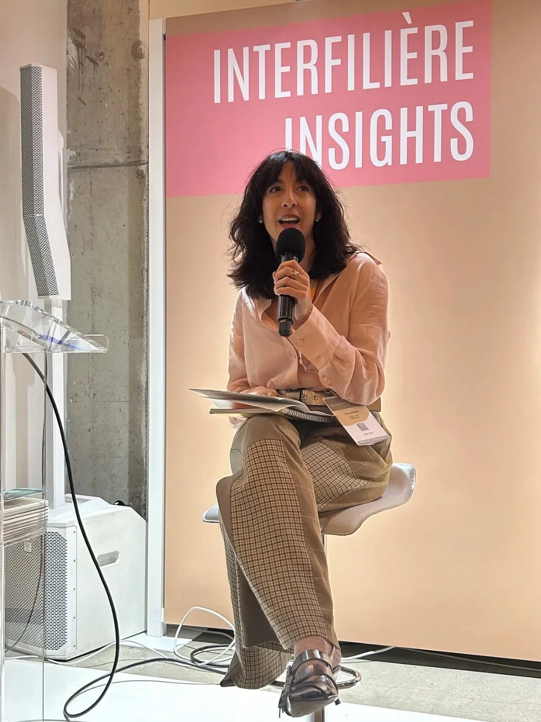 Woman with brown hair sitting in a stool with a microphone