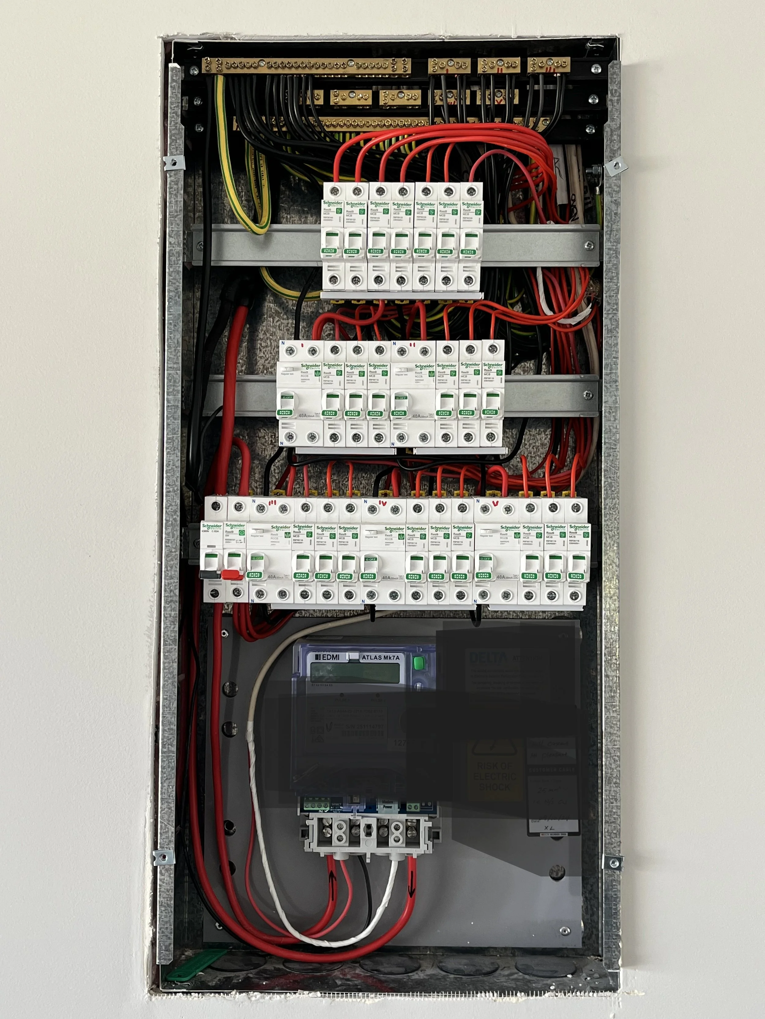 Electrical breaker panel with multiple circuit breakers, wiring, and a digital controller inside a metal enclosure.