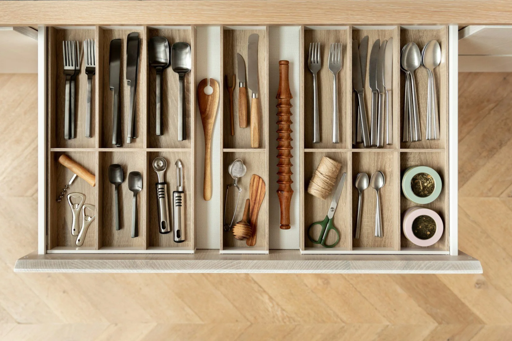 Organized drawer filled with various kitchen utensils and tools, including forks, knives, spoons, a corkscrew, scissors, and other cutlery.
