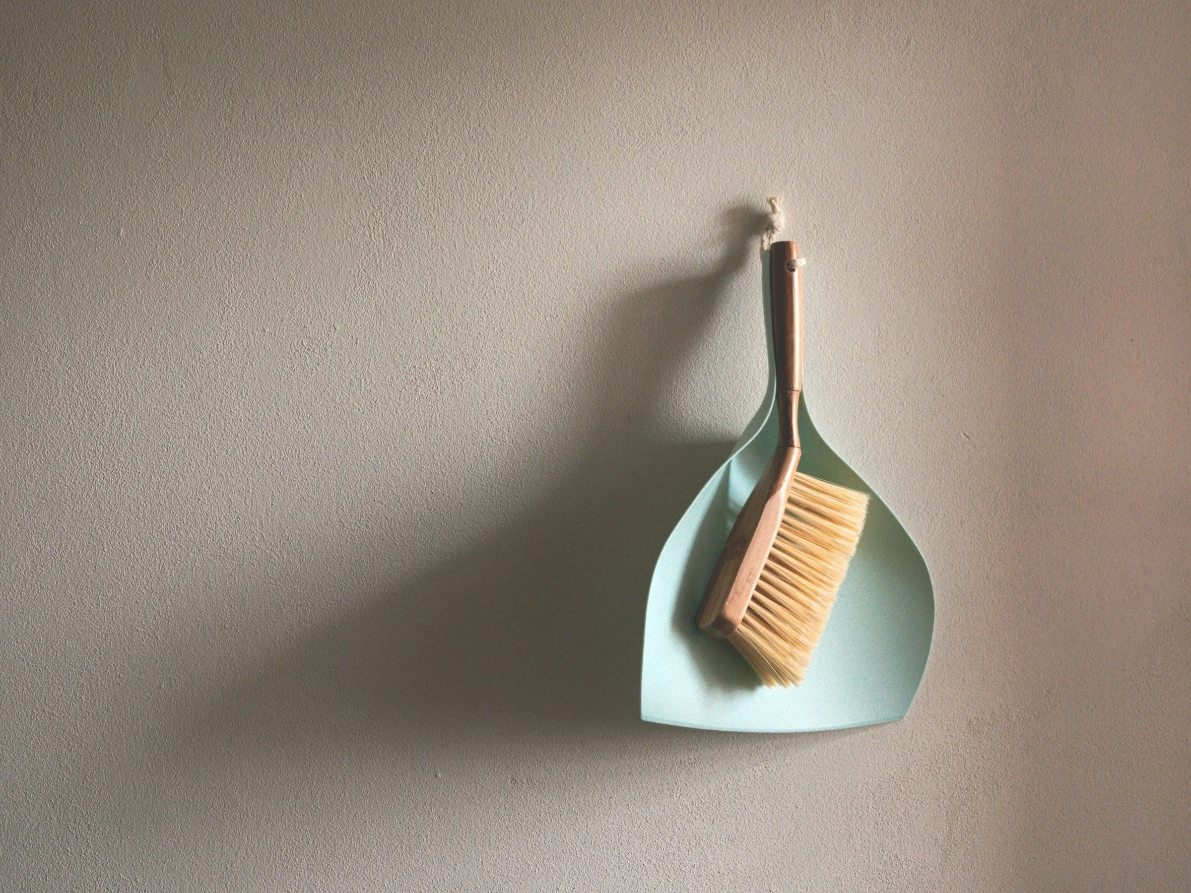 A small brush and dustpan hanging on a textured off-white wall.